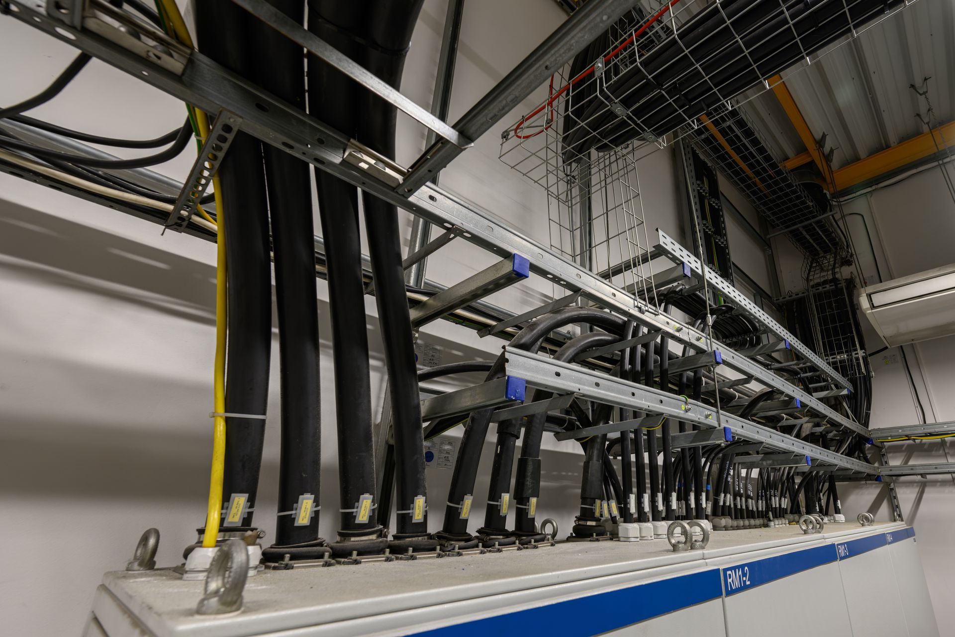 Rows of black cables in a server room, routed through overhead trays above white equipment.