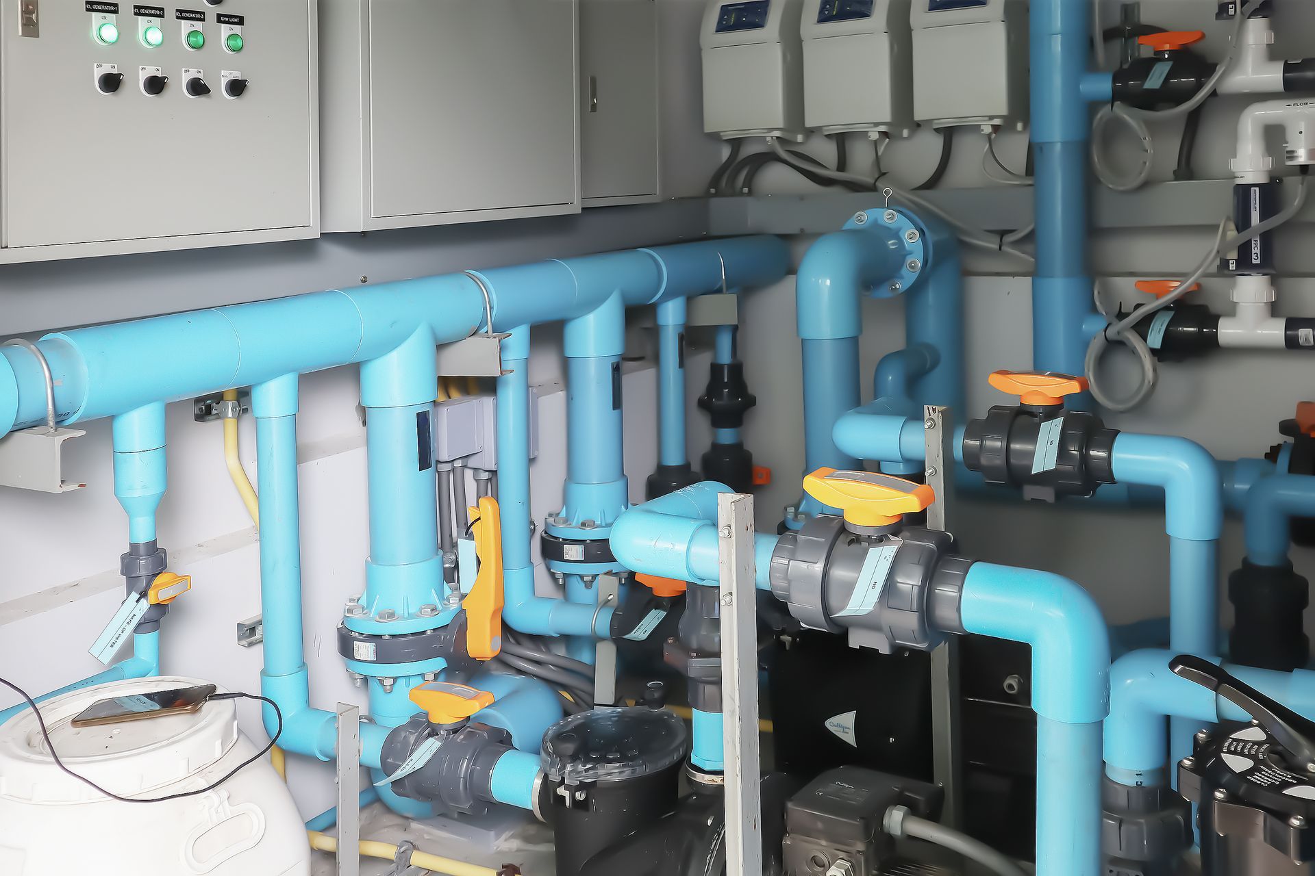 Blue industrial piping and pumps inside a mechanical room with control panels and valves.