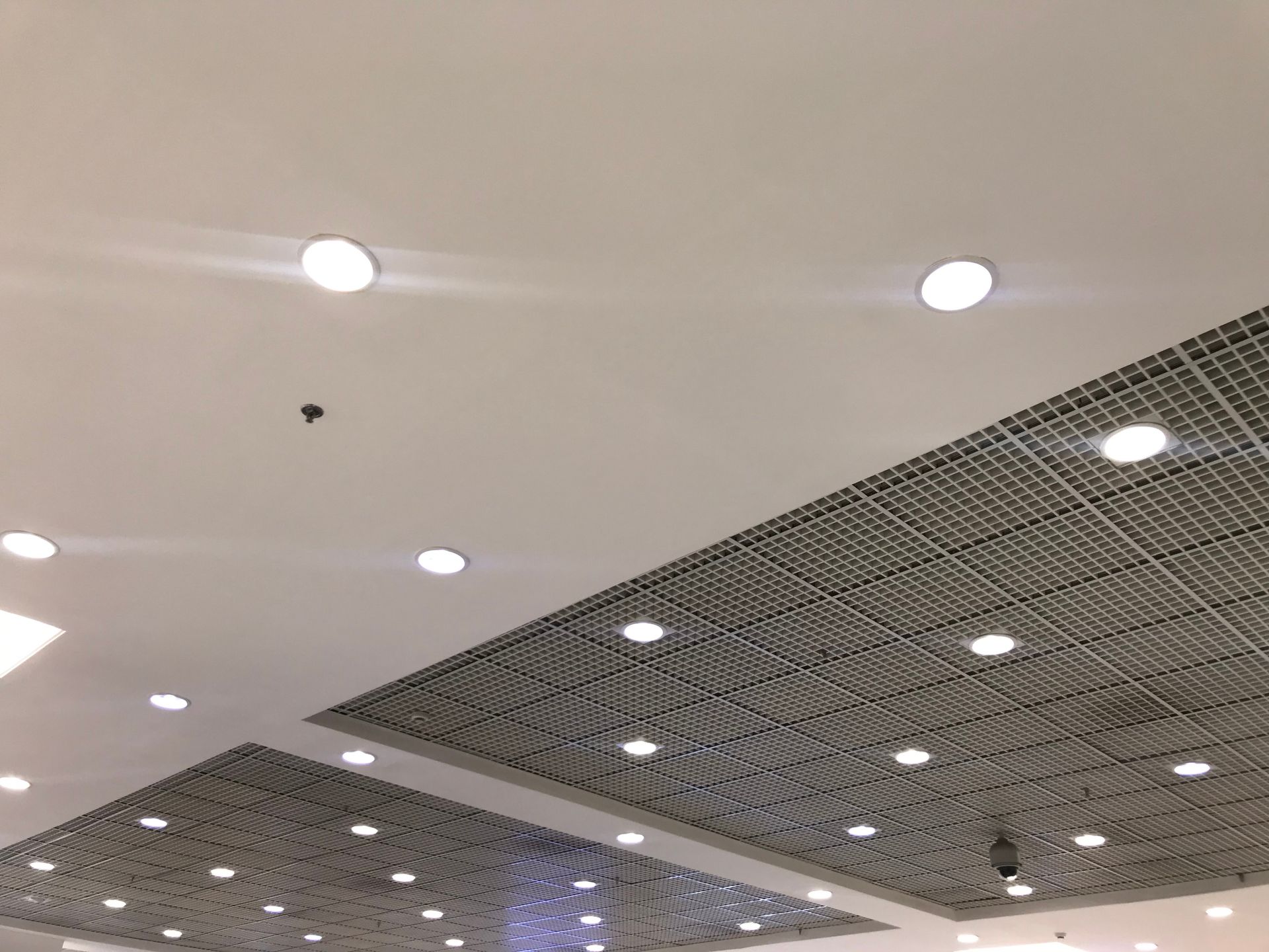 Ceiling with recessed lights and a large dark mesh panel in a modern indoor space.