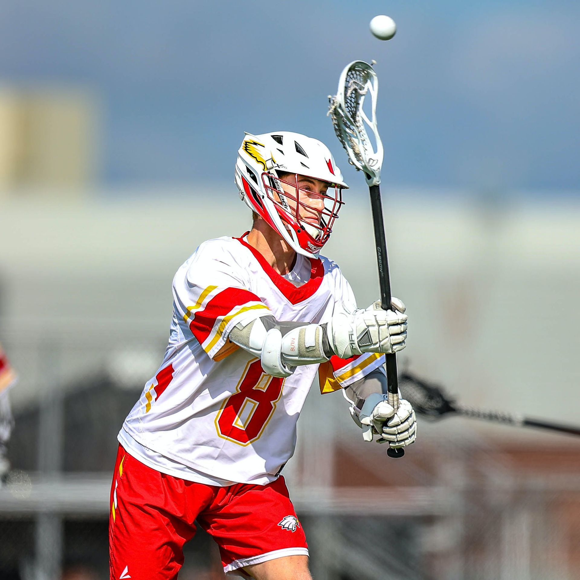 Lacrosse player in white and red jersey catching a pass with a lacrosse stick