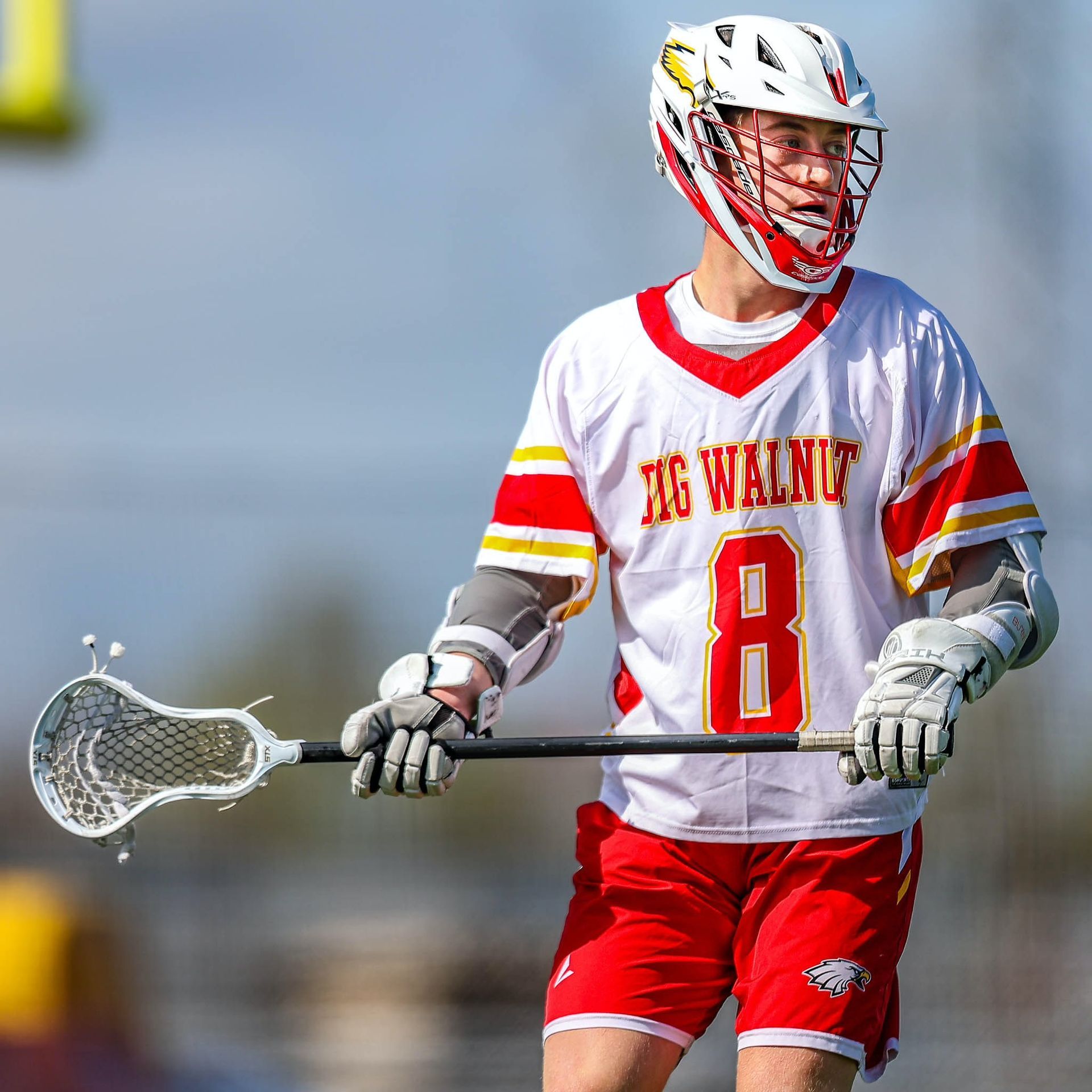 Lacrosse player in white and red uniform holding a stick on a field