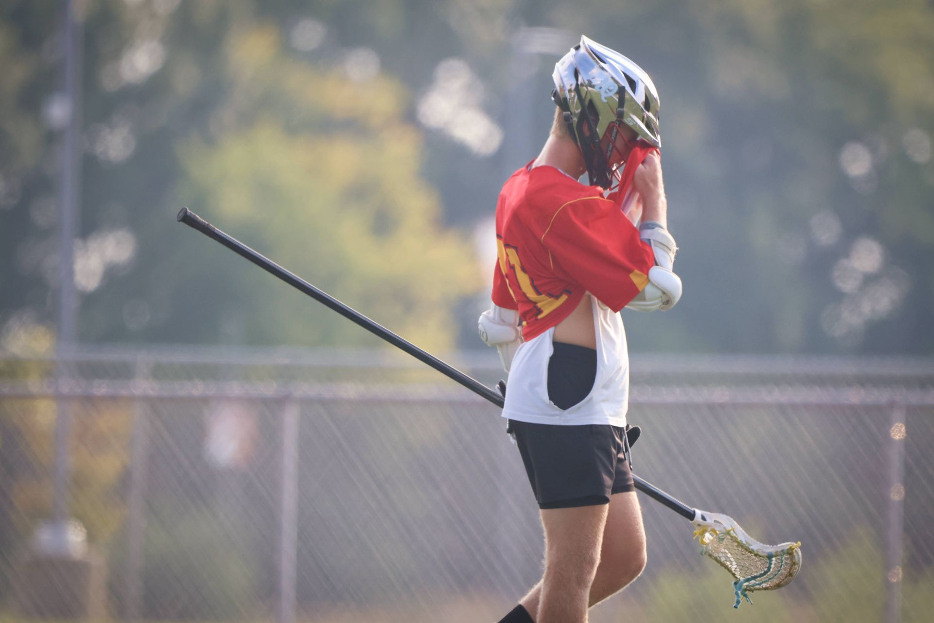 Lacrosse player in red jersey standing on a field with a stick resting on their shoulder