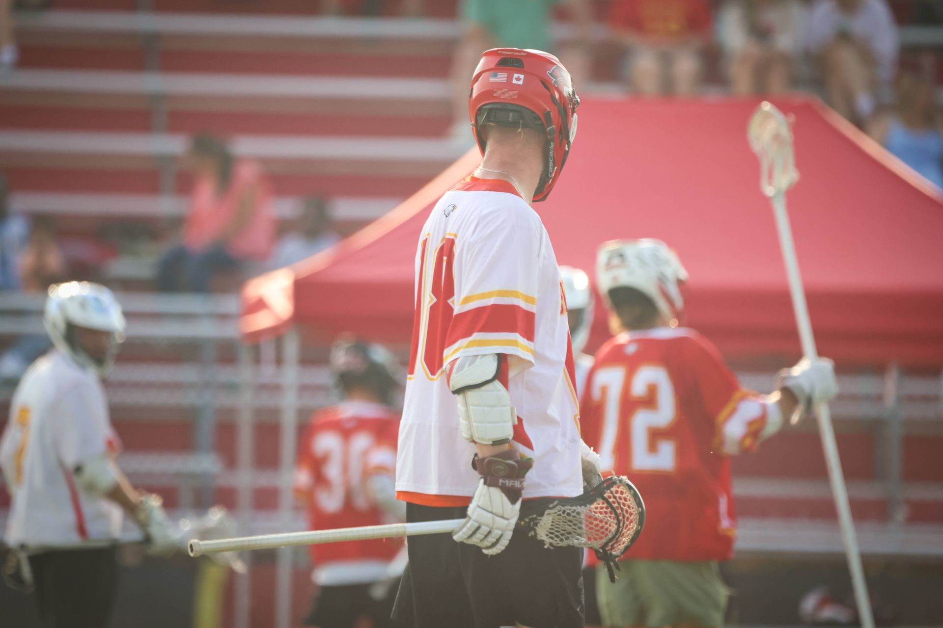 Lacrosse players in red and white uniforms on a field near the sideline bench
