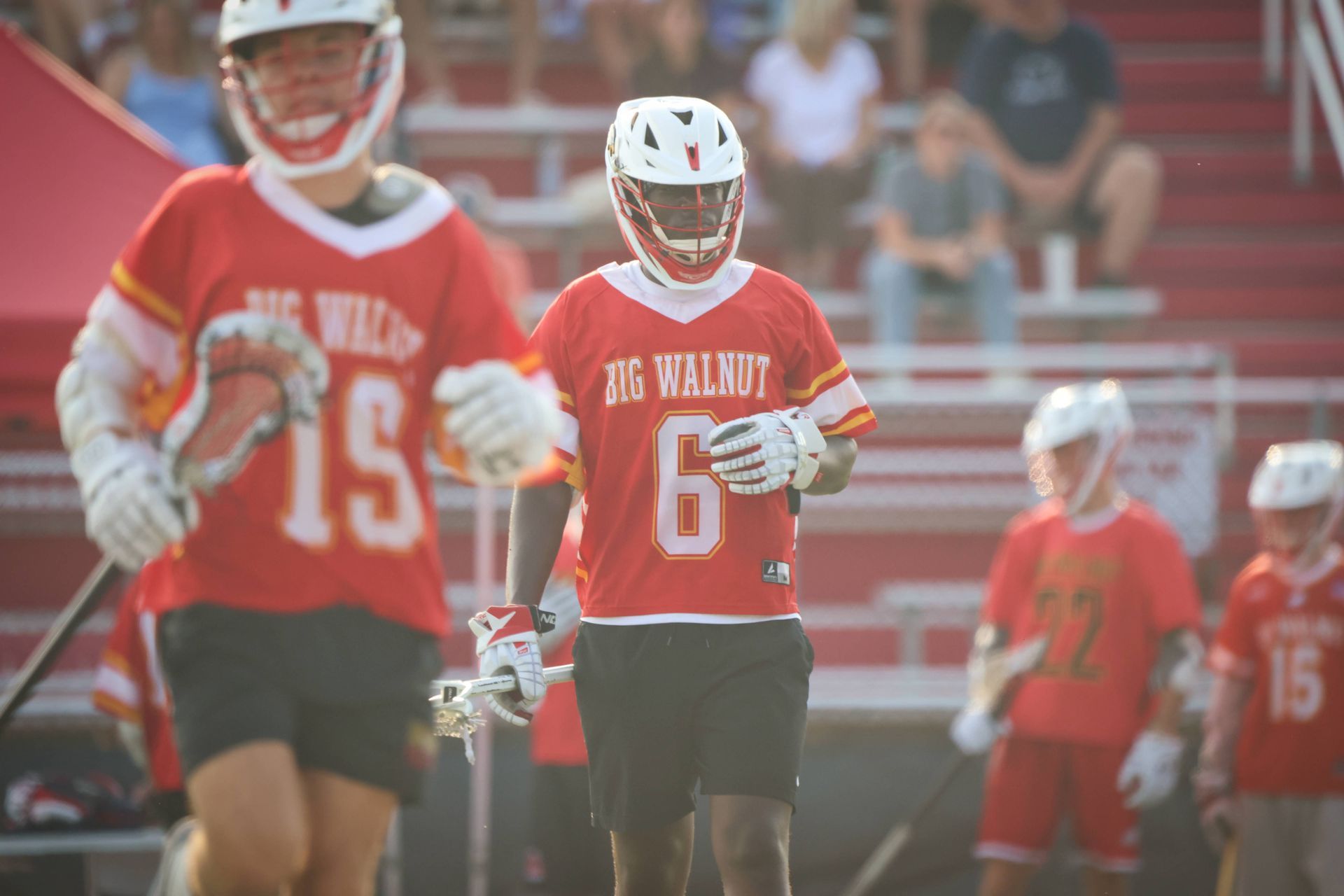 Lacrosse players in red jerseys on a field, with one holding a stick in the foreground.