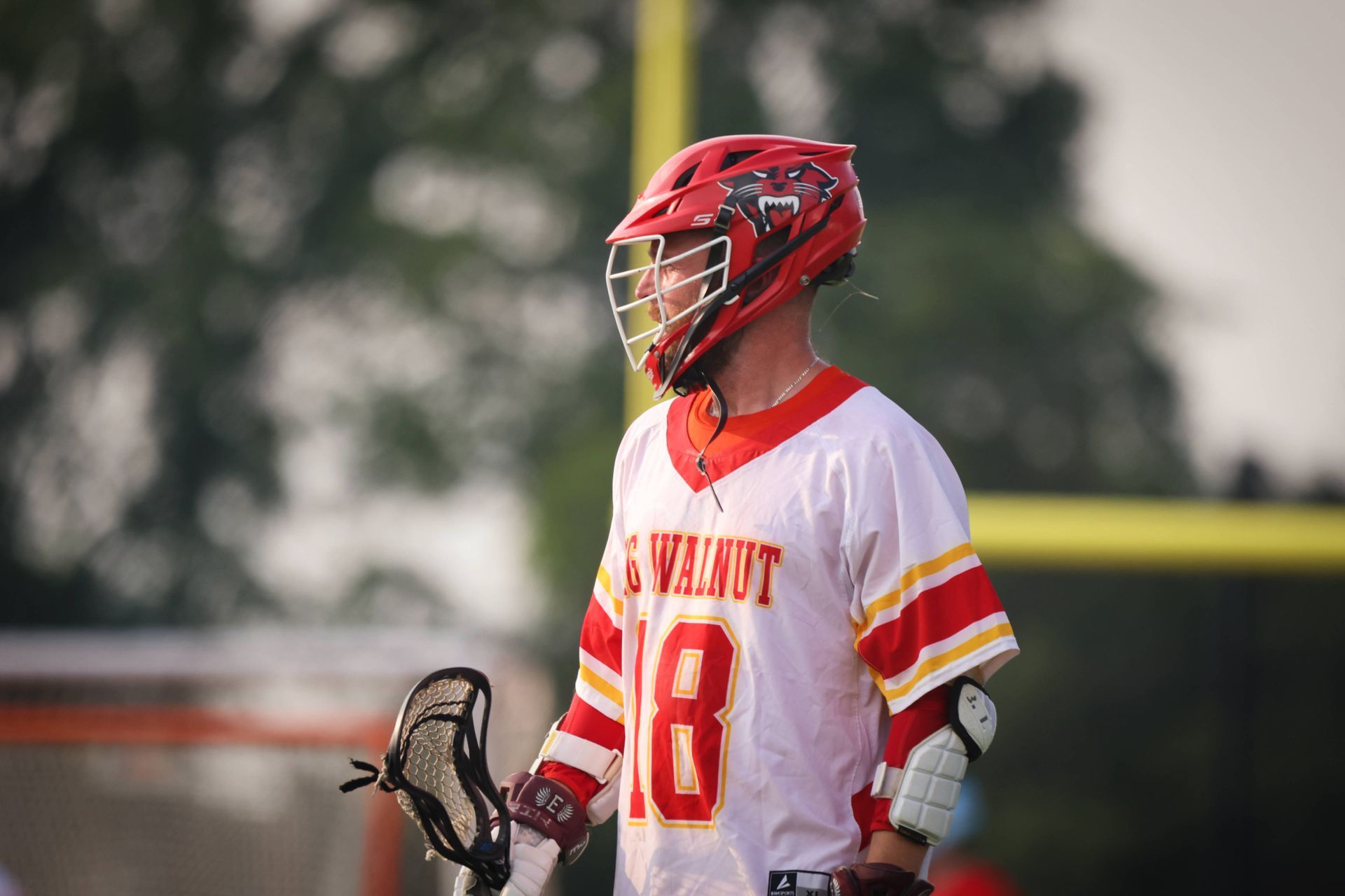 Lacrosse player in red helmet and white jersey with number 18 holding a stick on the field