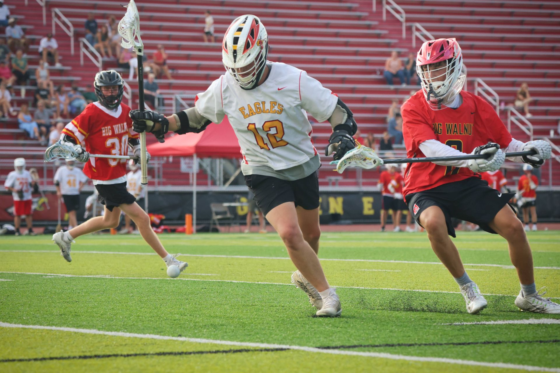 Lacrosse players in red and white sprint on a green turf field during a game