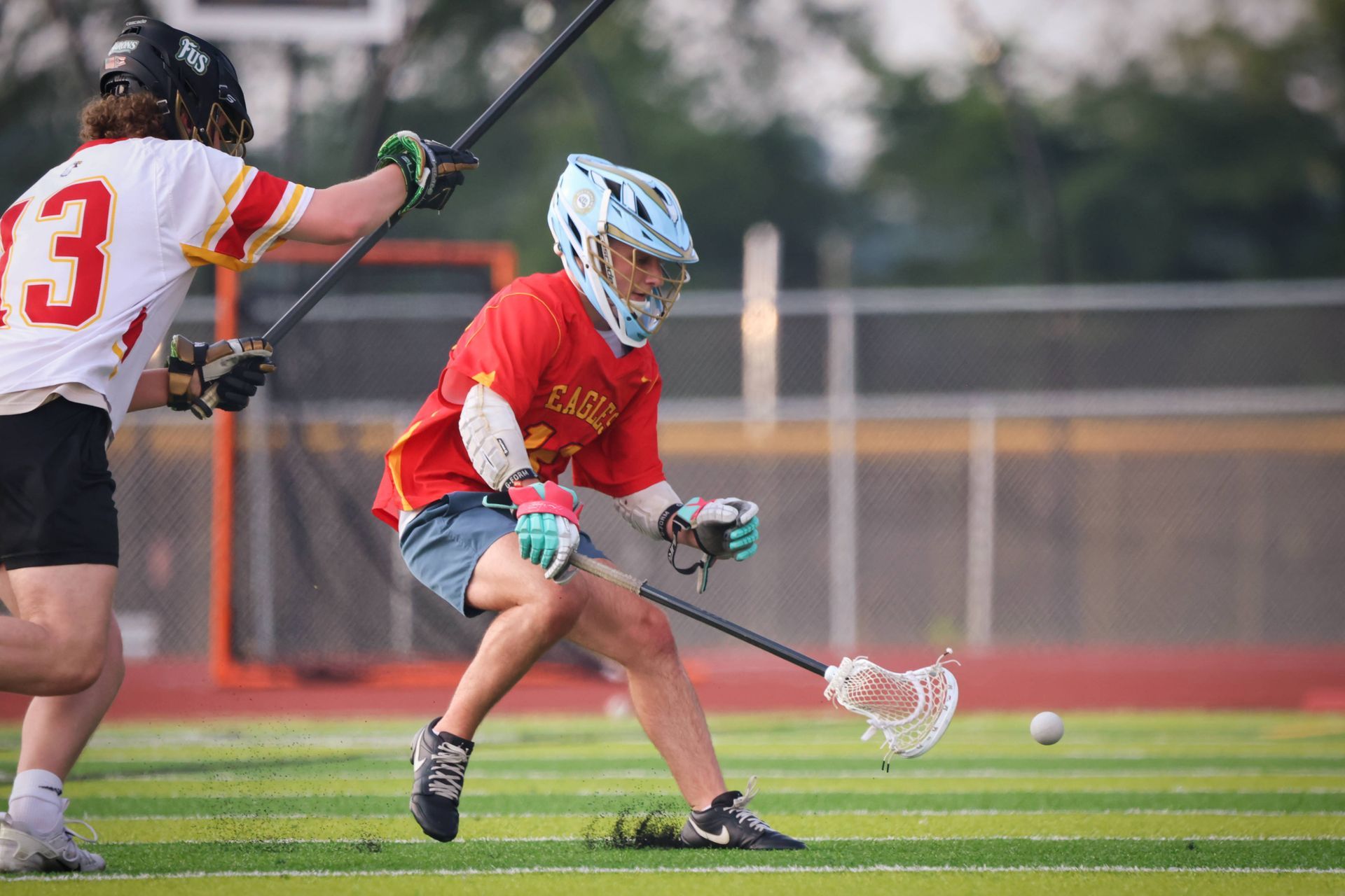 Two lacrosse players in red jerseys chase a ball on a field during a game
