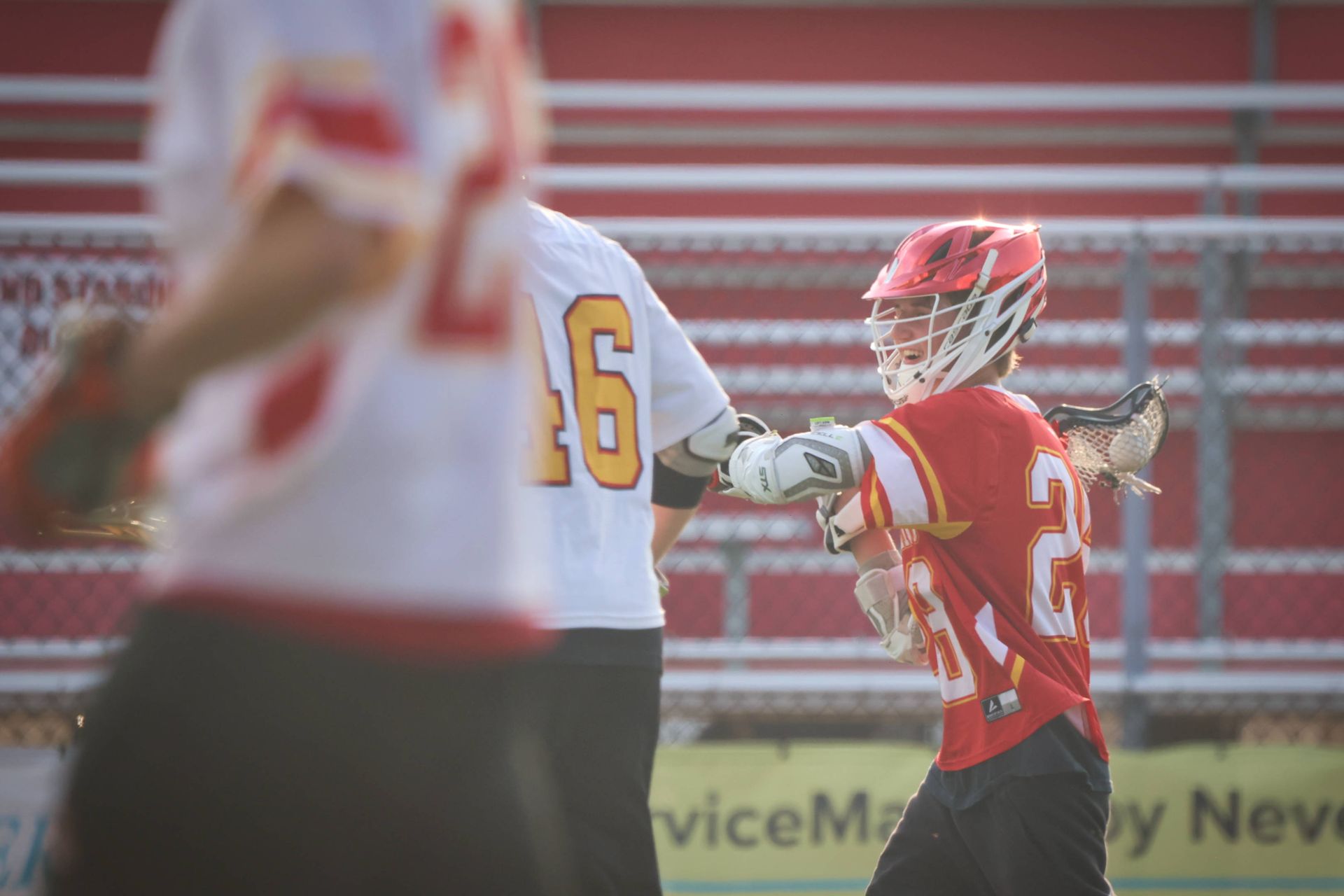 Lacrosse players in red and white uniforms compete on a field during a game.
