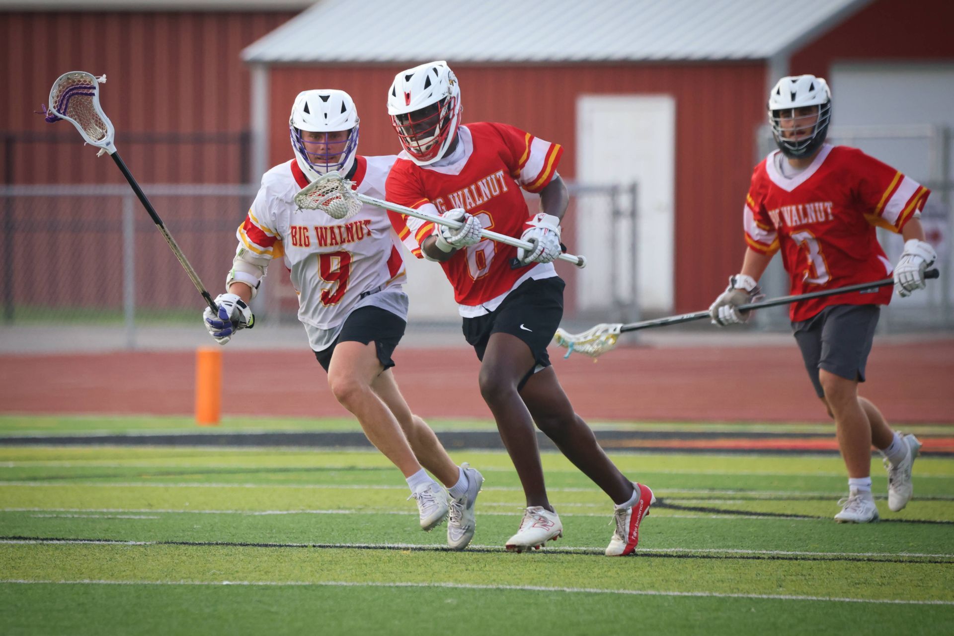 Three lacrosse players in red and white uniforms running on a field during a game