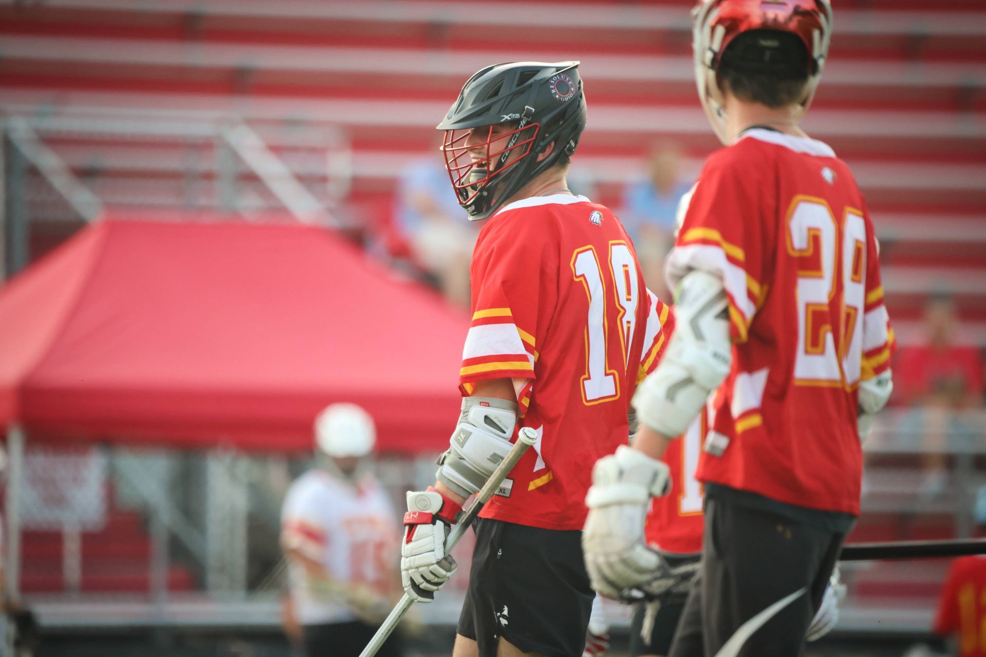Two lacrosse players in red jerseys standing on a field near a red tent