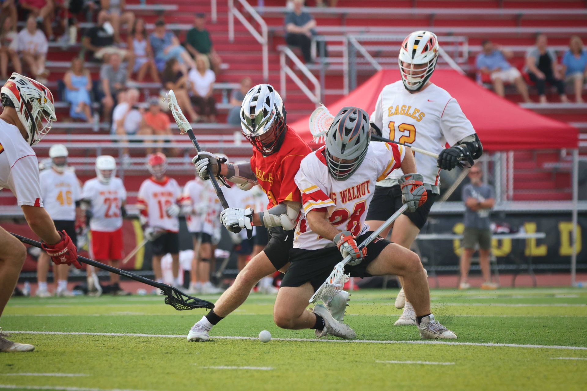 Lacrosse player in red shoots on goal while defenders in white converge on a grass field