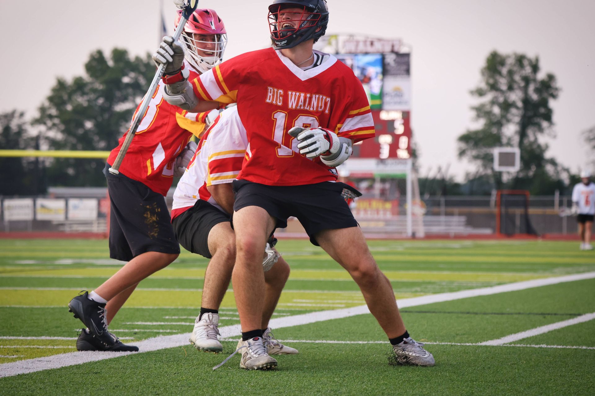 Two lacrosse players in red jerseys on a field, one cradling the ball during play