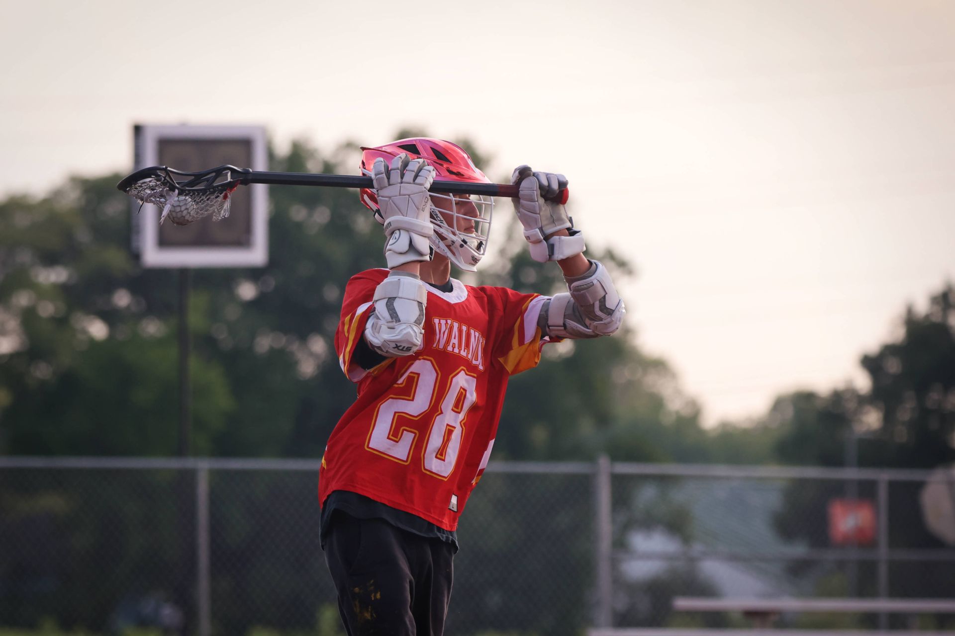 Lacrosse player in red jersey catches a pass with the goal and field in the background