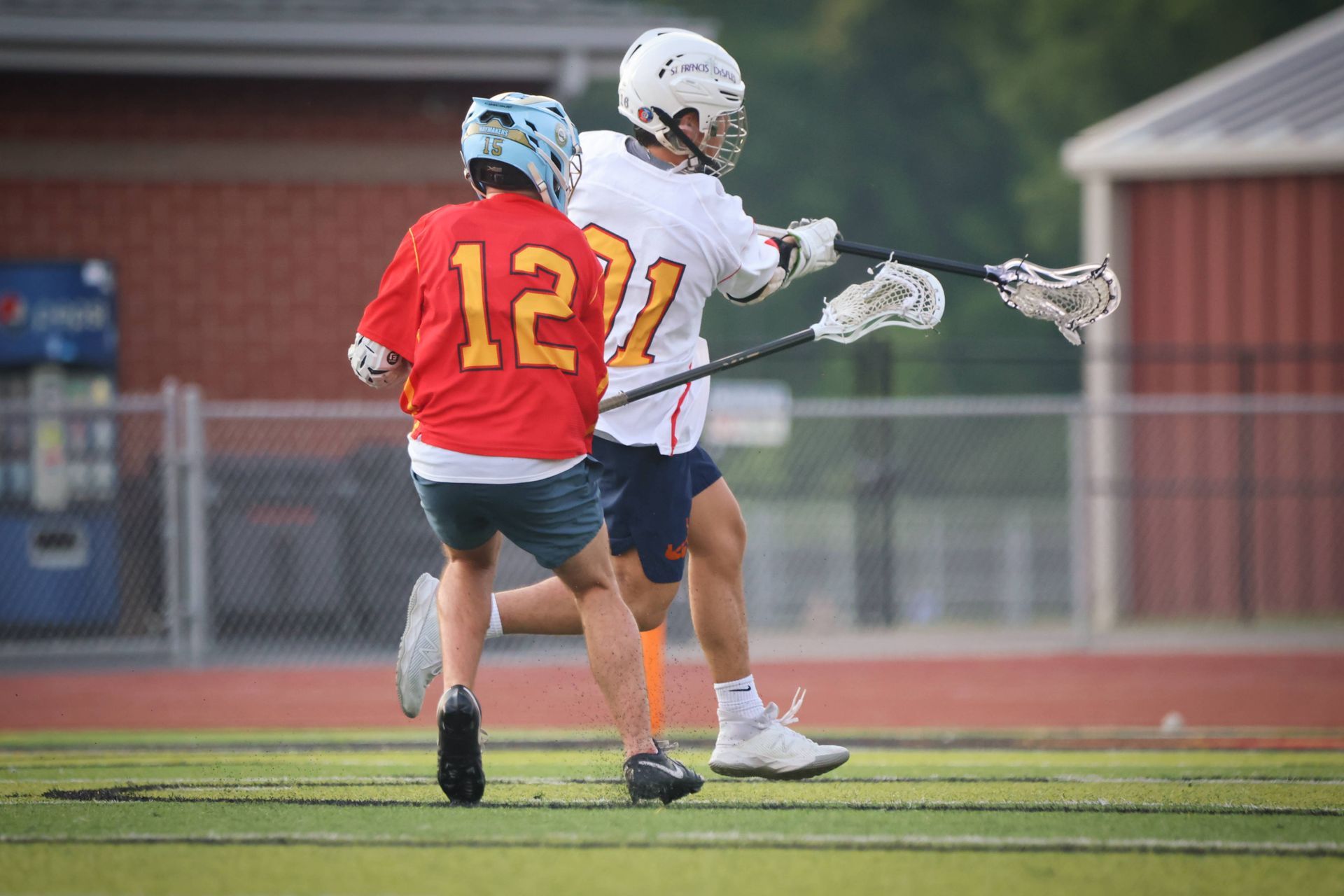 Two lacrosse players in red and white jerseys compete on a field