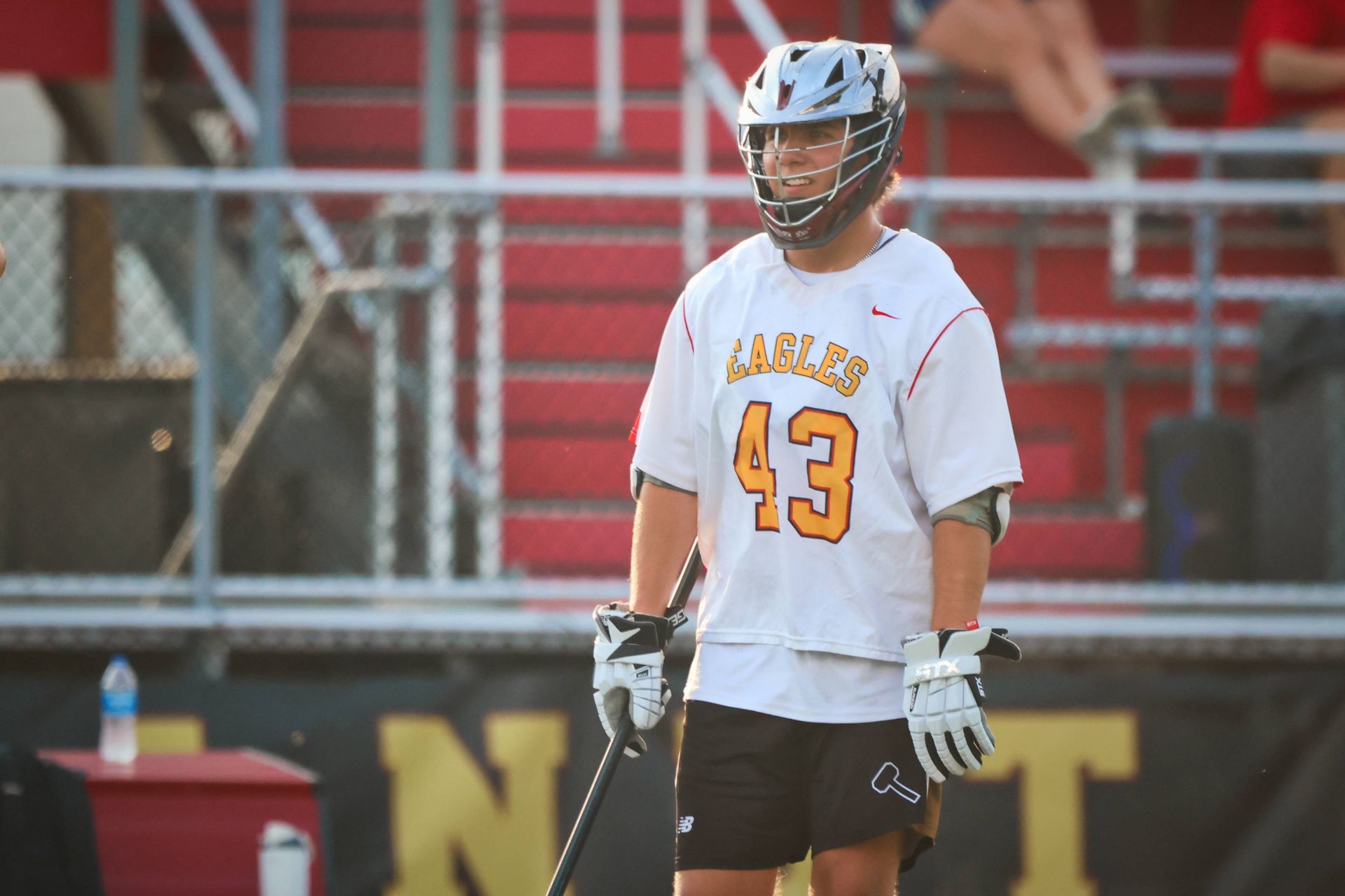 Lacrosse player in white jersey number 43 stands on the field holding a stick.