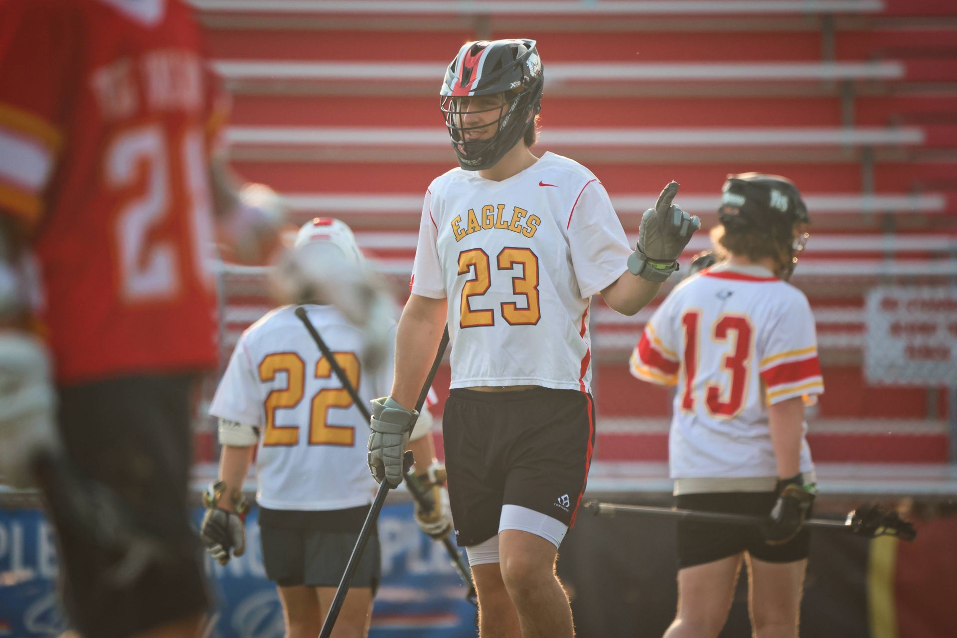 Lacrosse players in white and red uniforms standing on a field with bleachers in the background