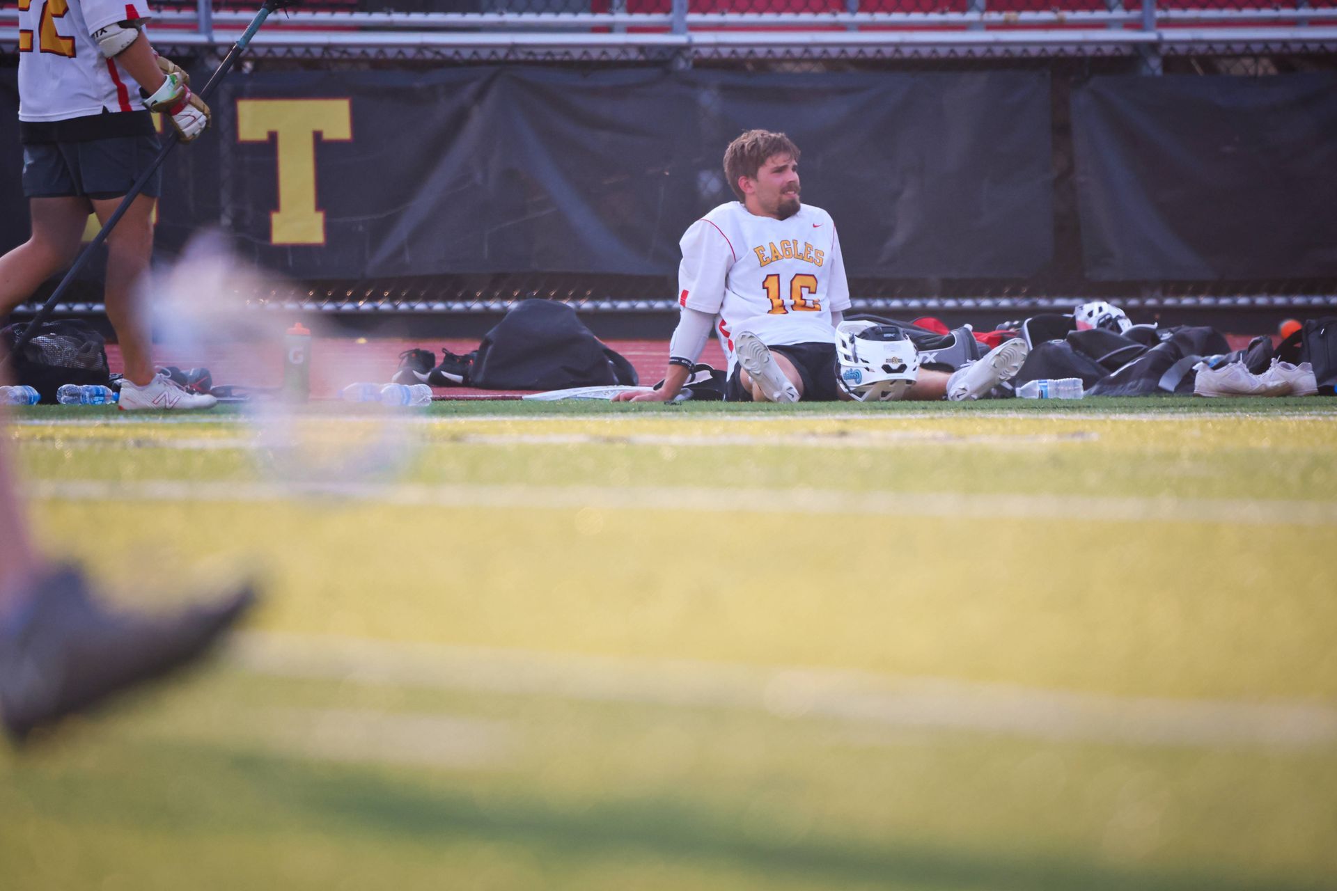 Lacrosse player sitting on the field with a blurred player in the foreground