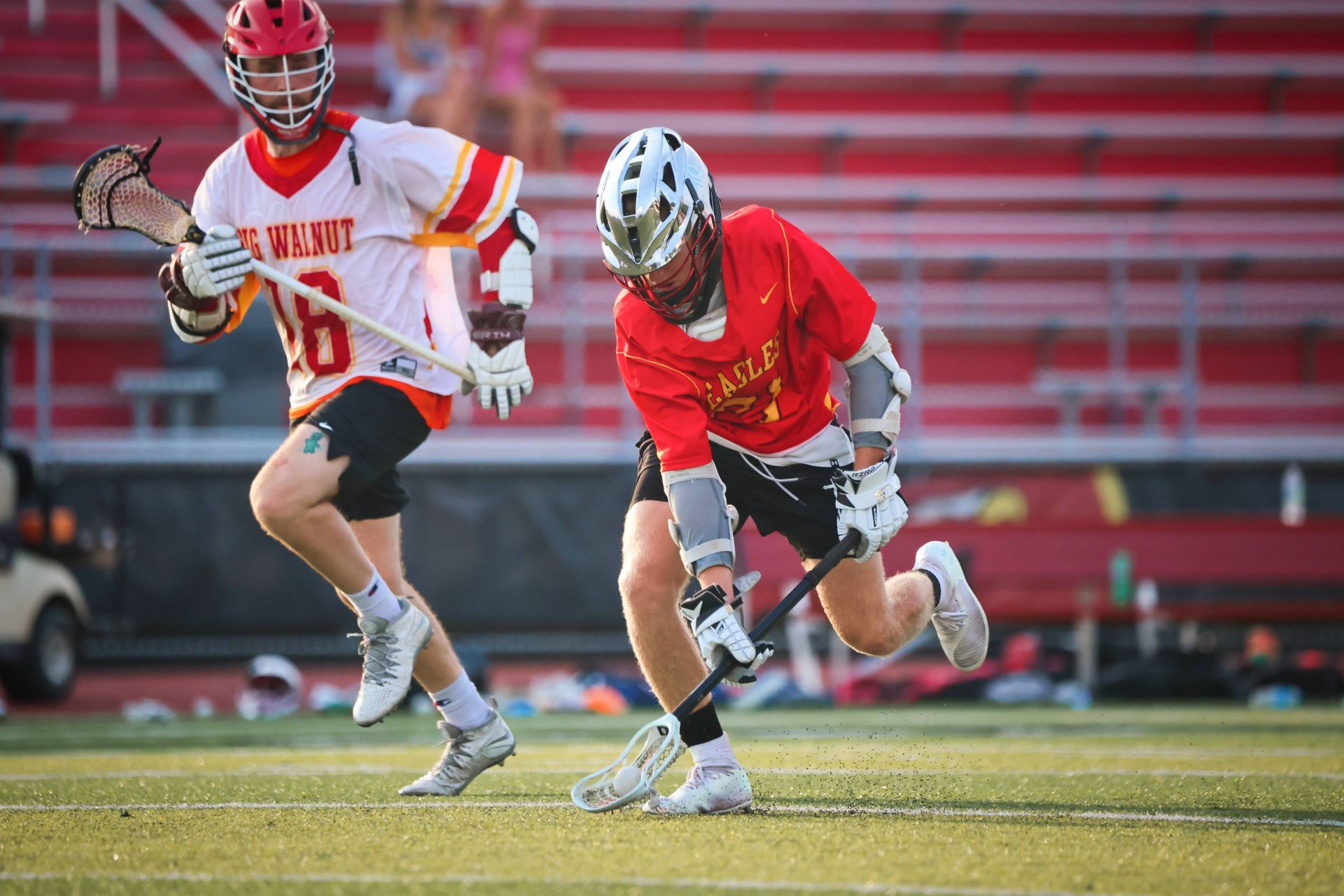 Two lacrosse players in red and white uniforms running on a field during play