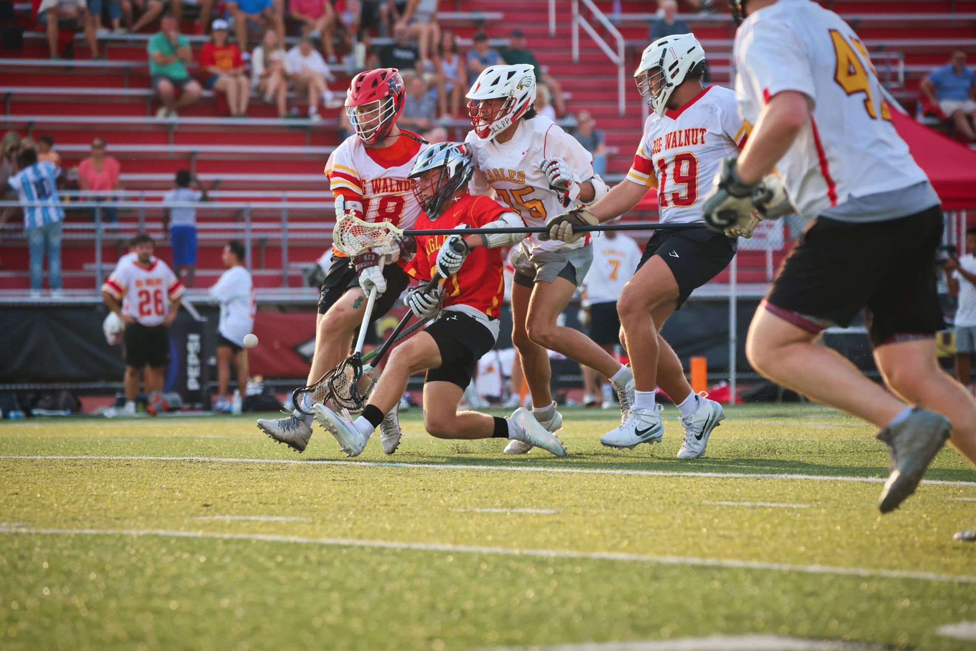 Lacrosse players in white and red jerseys sprinting on a field during a game.