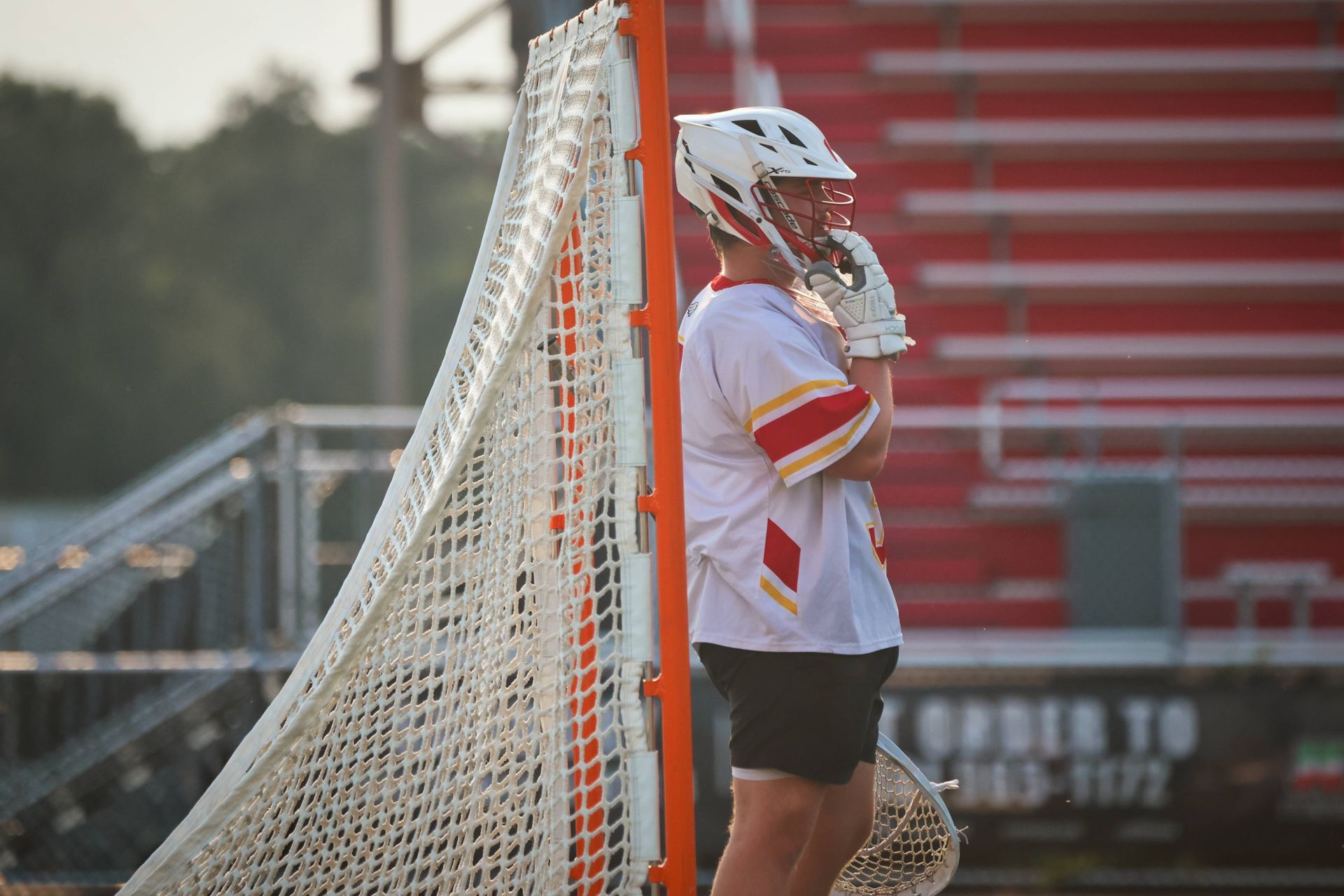 Lacrosse player in white uniform stands beside the goal net on the field.
