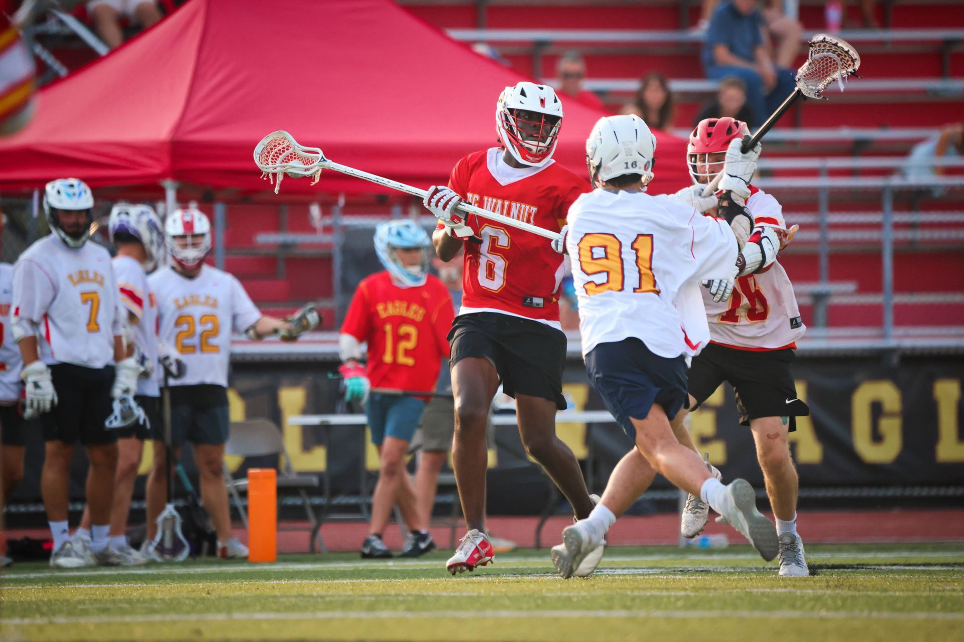 Lacrosse players in red and white uniforms jump for a shot near the goal on a field