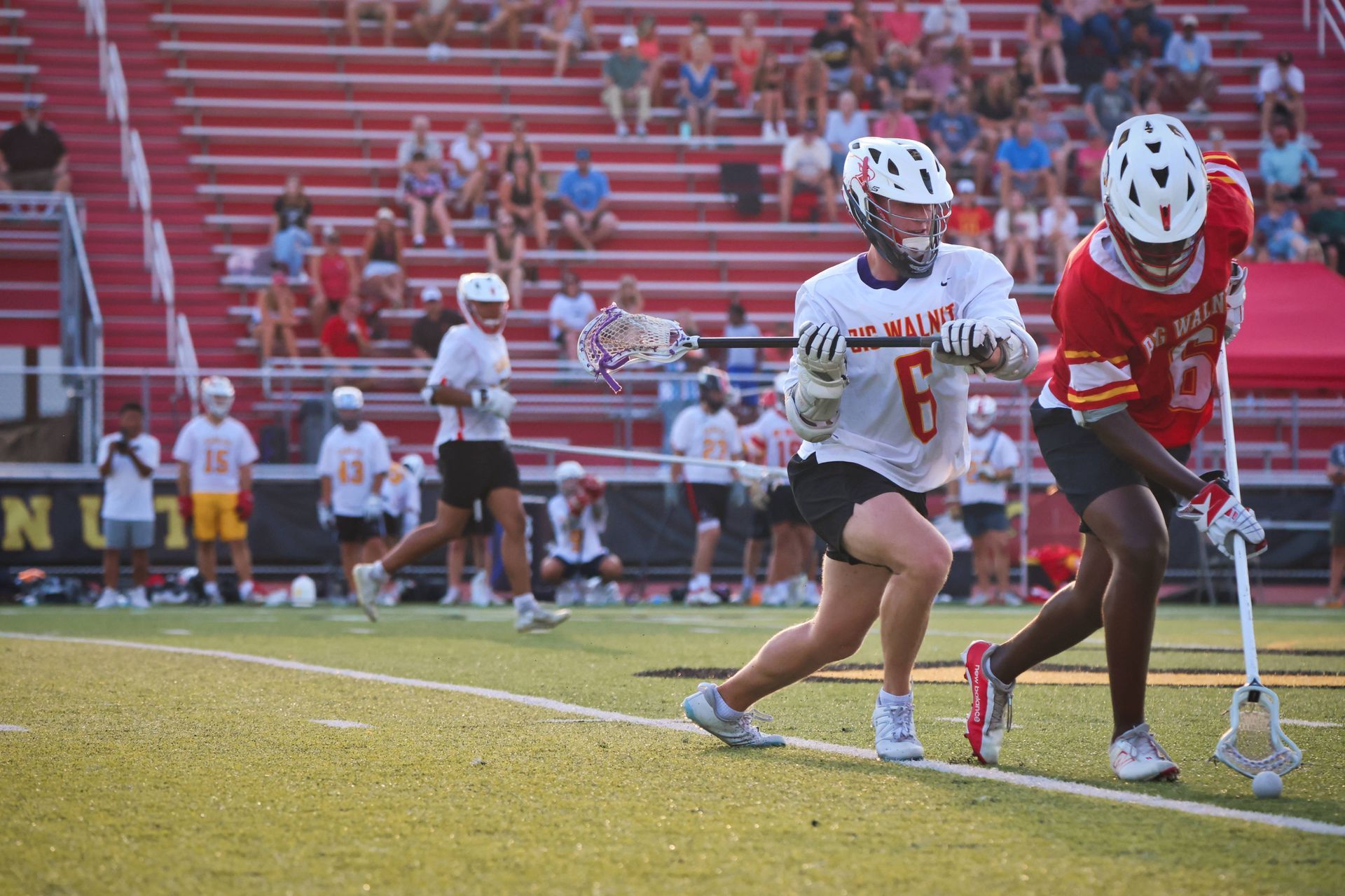 Two lacrosse players in red and white uniforms running on a field during a game