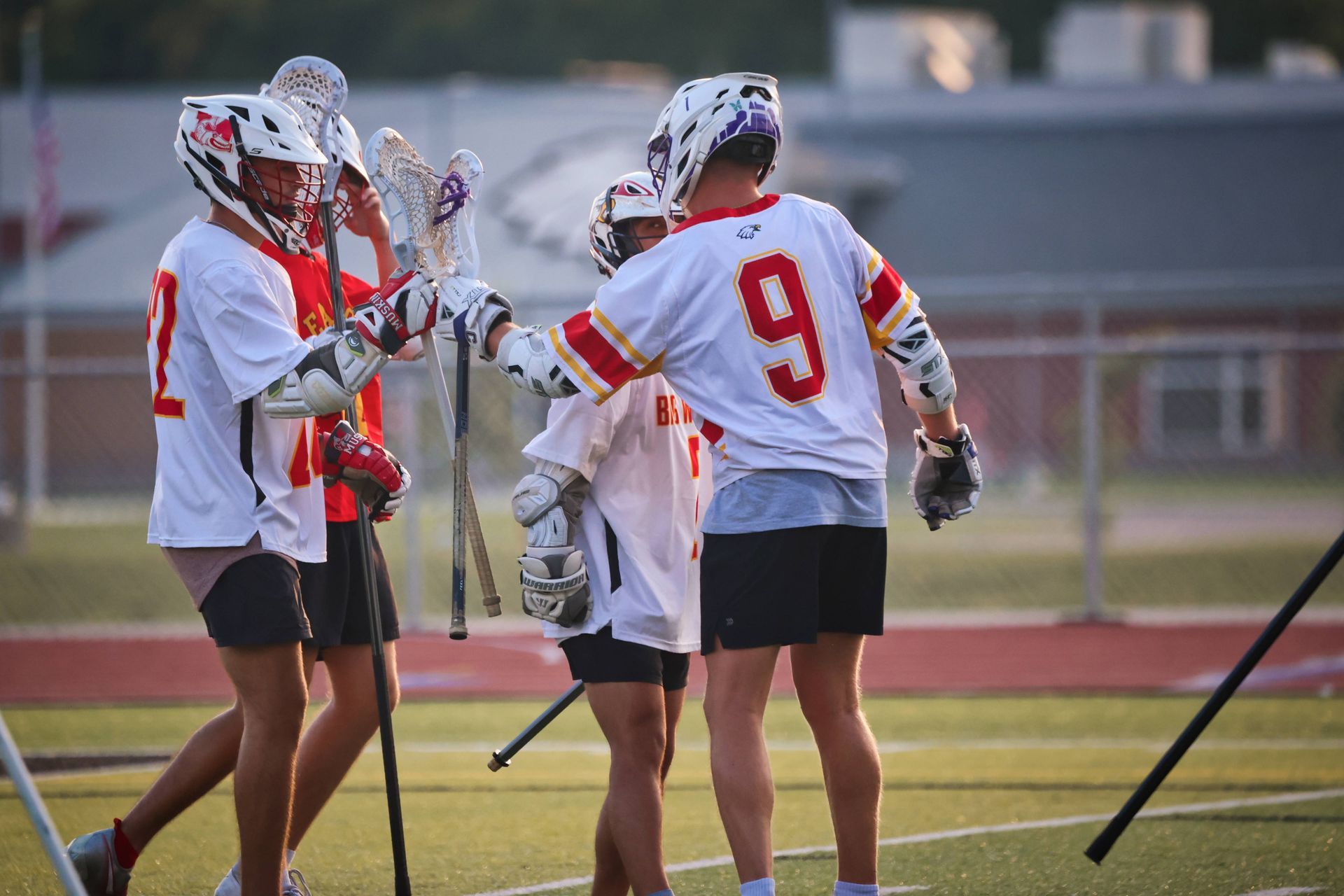 Lacrosse players in white and red uniforms huddle on a field during practice or a game