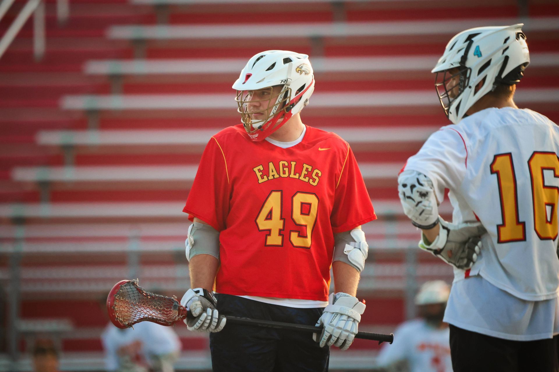 Two lacrosse players in helmets on a field, one in a red Eagles jersey holding a stick.