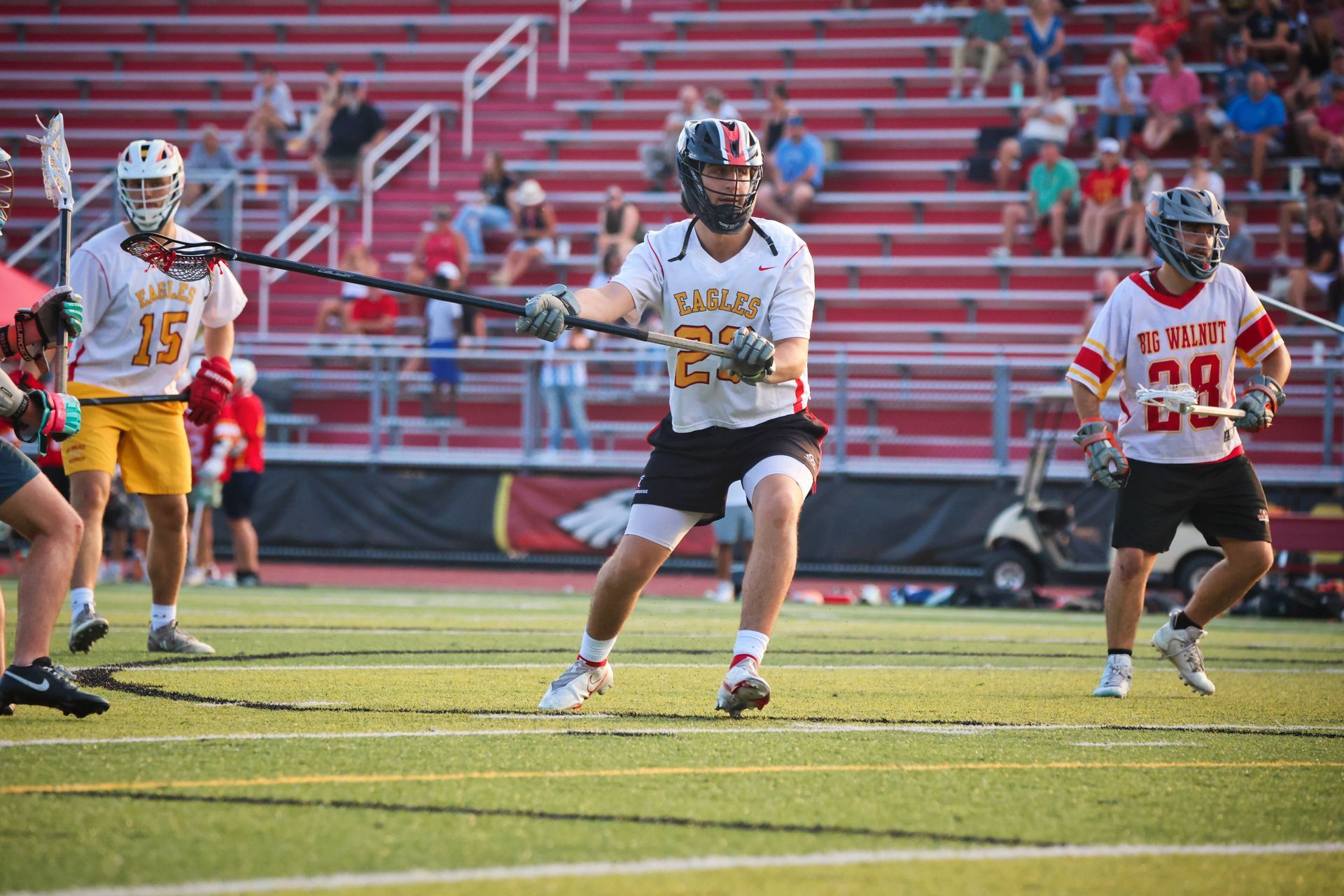 Three lacrosse players in white and red uniforms run on a field during a game