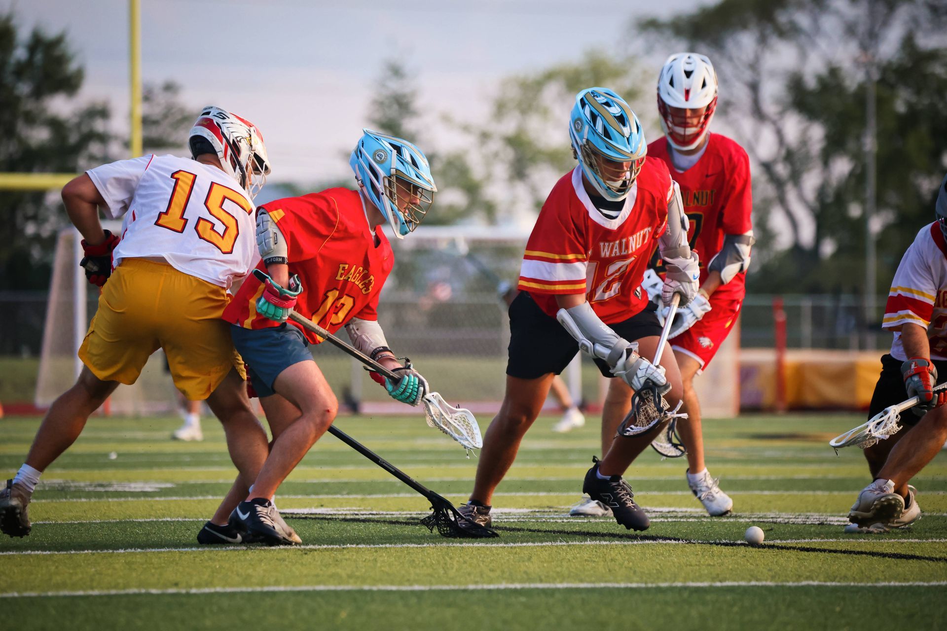 Lacrosse players in red and white uniforms battling for the ball on a grassy field