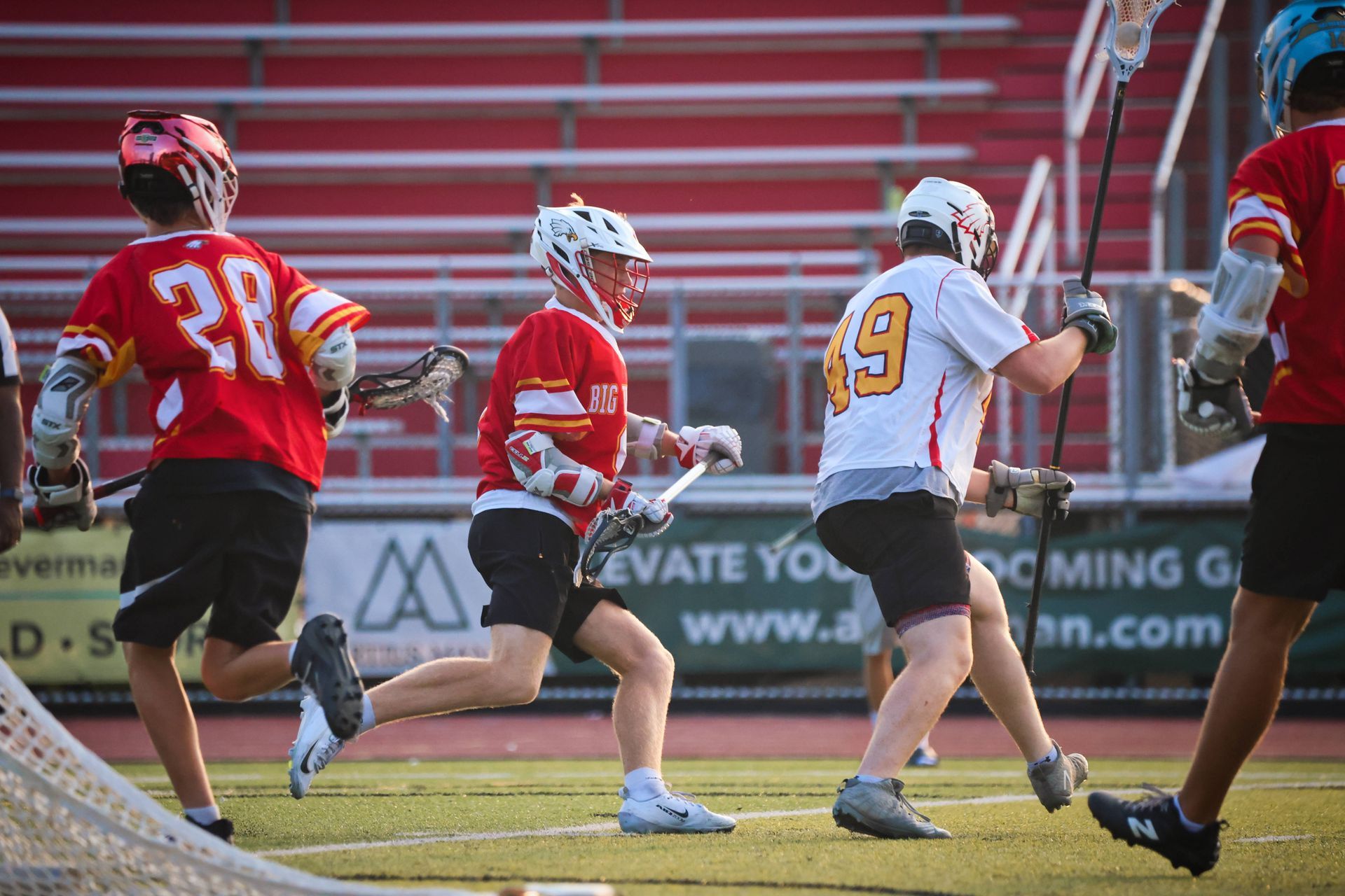 Lacrosse players in red and white uniforms run on a field during a game.