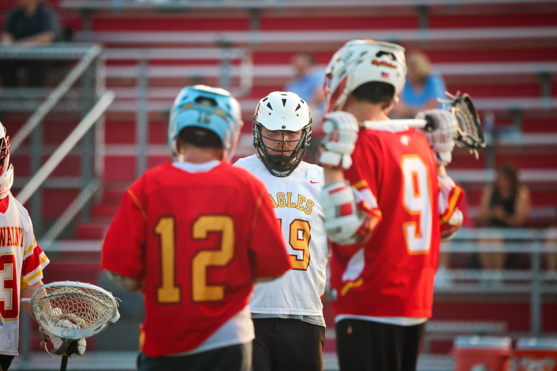 Lacrosse players in red and white uniforms on a field during a game, with one player centered in focus