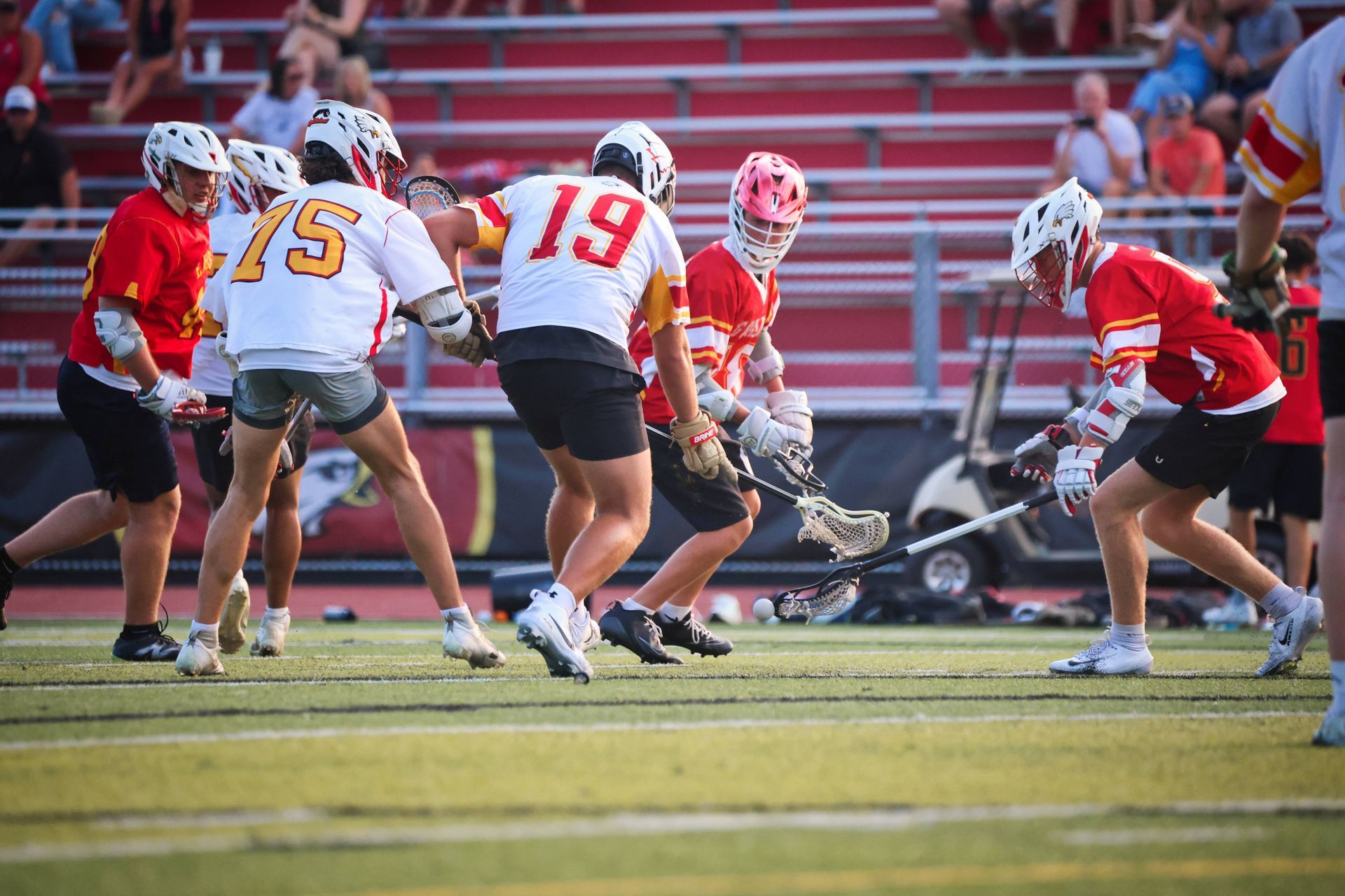 Lacrosse players in white and red uniforms battle for the ball on a field.