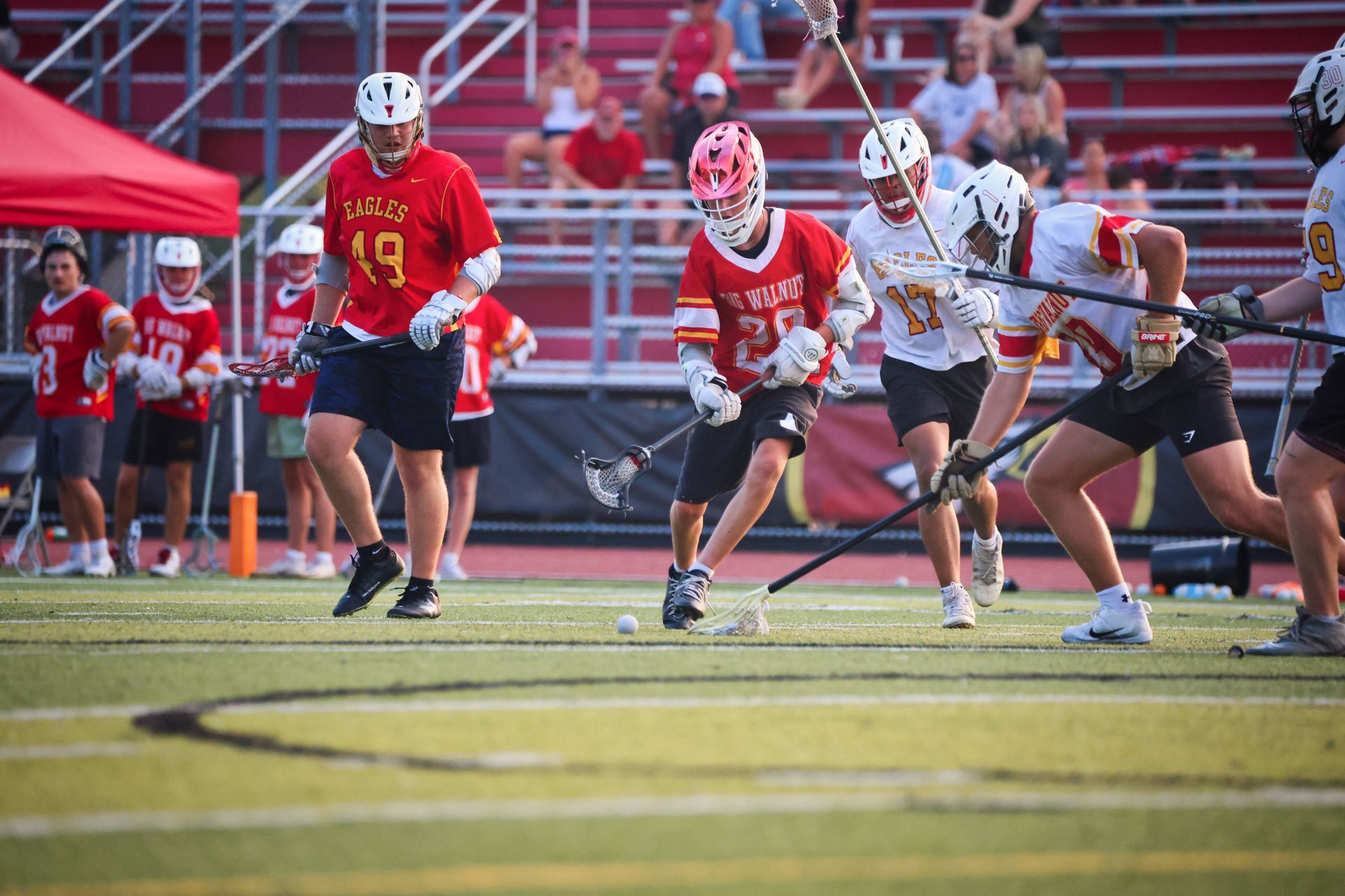Lacrosse players in red and white uniforms sprint on a field during a game.
