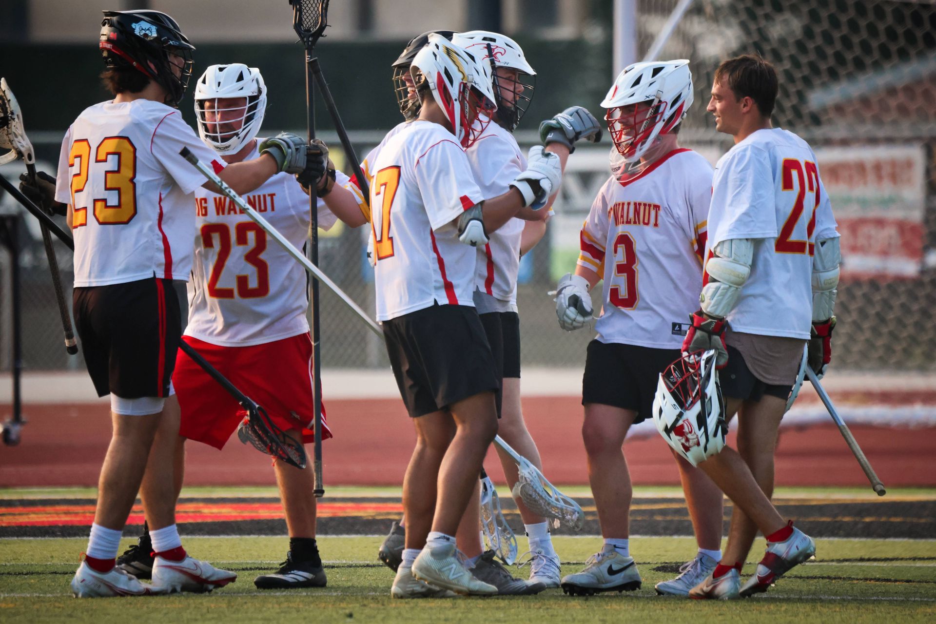Lacrosse players in white jerseys huddle on the field during a game