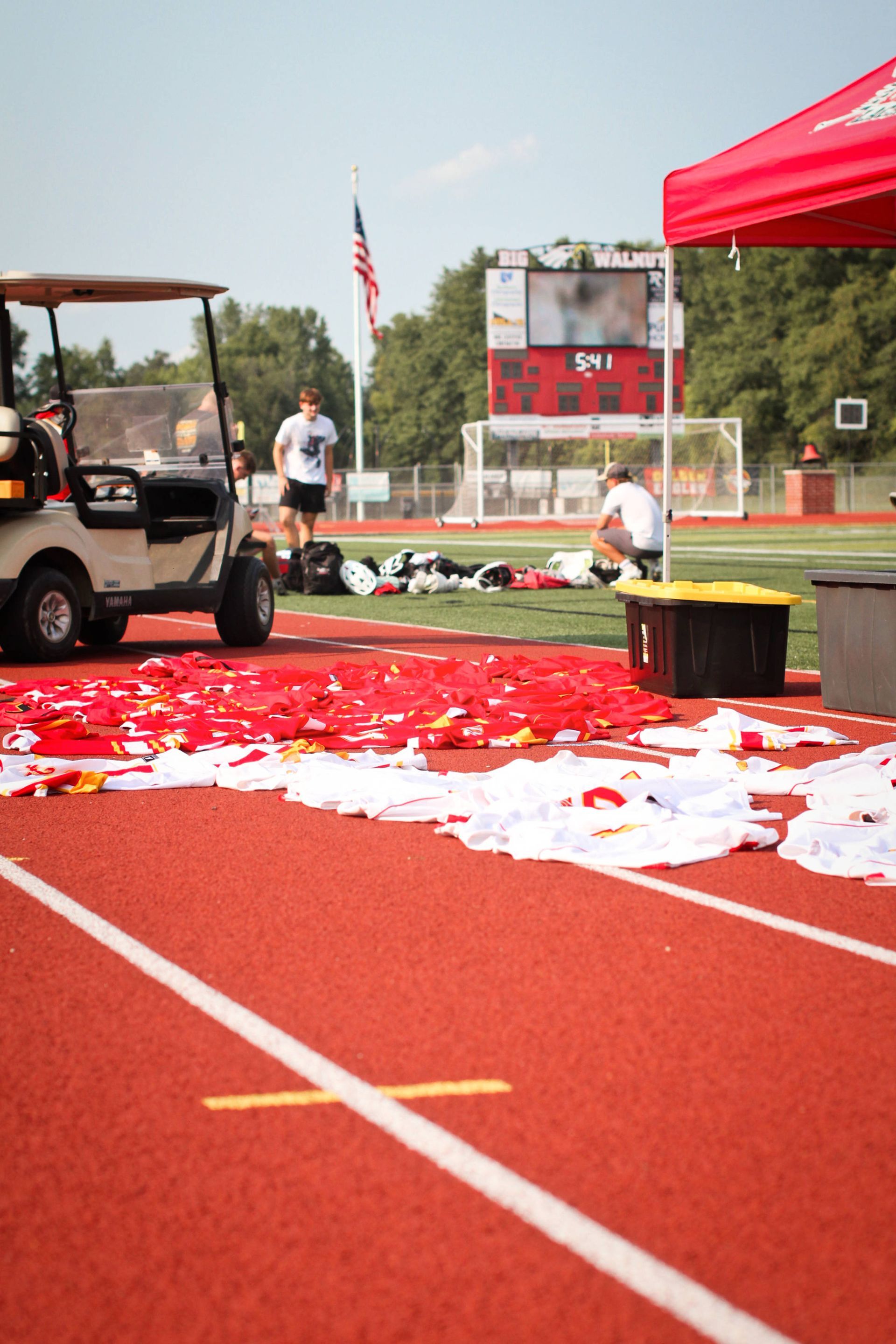Lacrosse field with scattered red and white confetti, a golf cart, and a scoreboard at an outdoor event