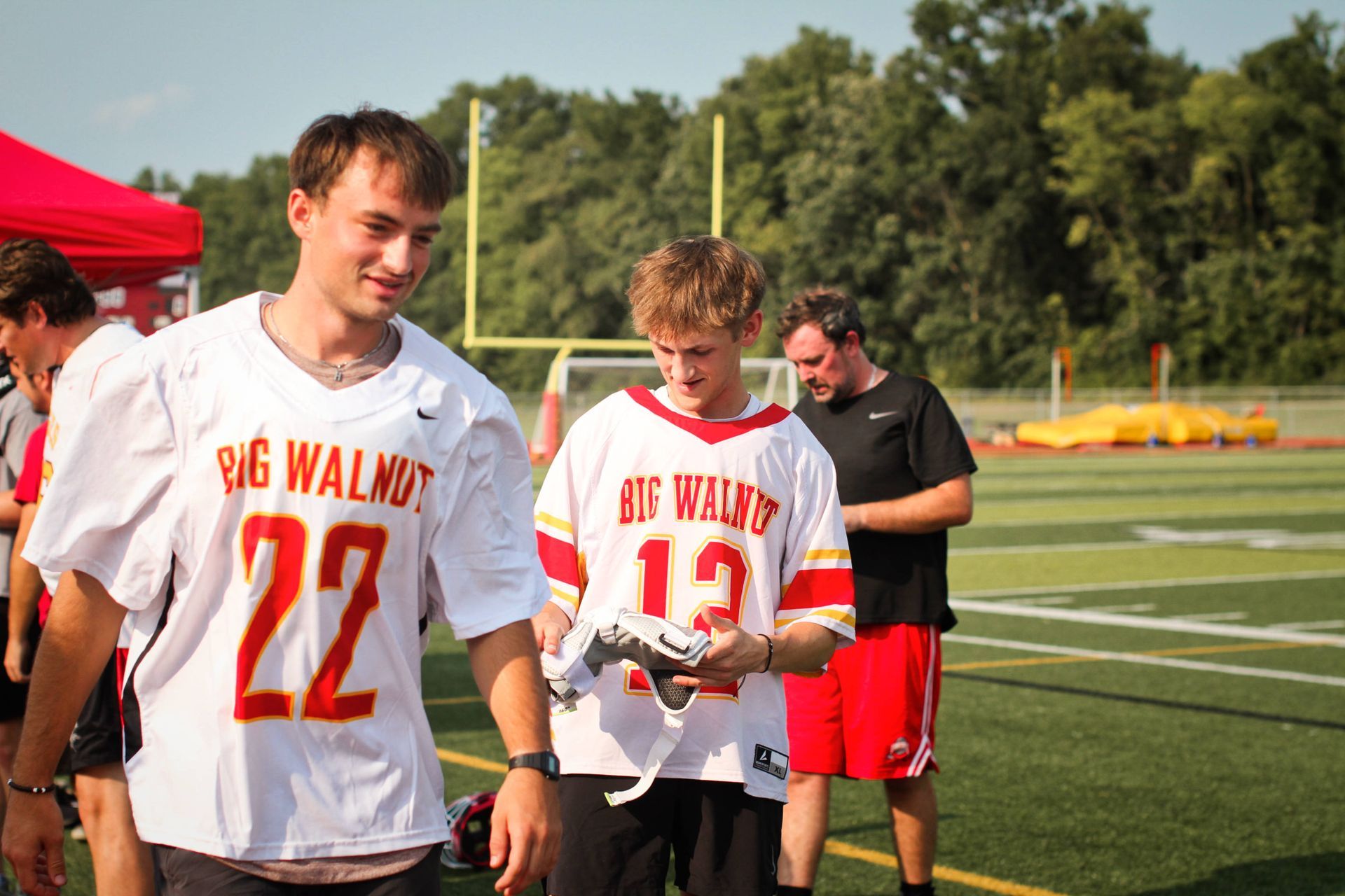 Athletes in white and red jerseys walk on a lacrosse field during practice.
