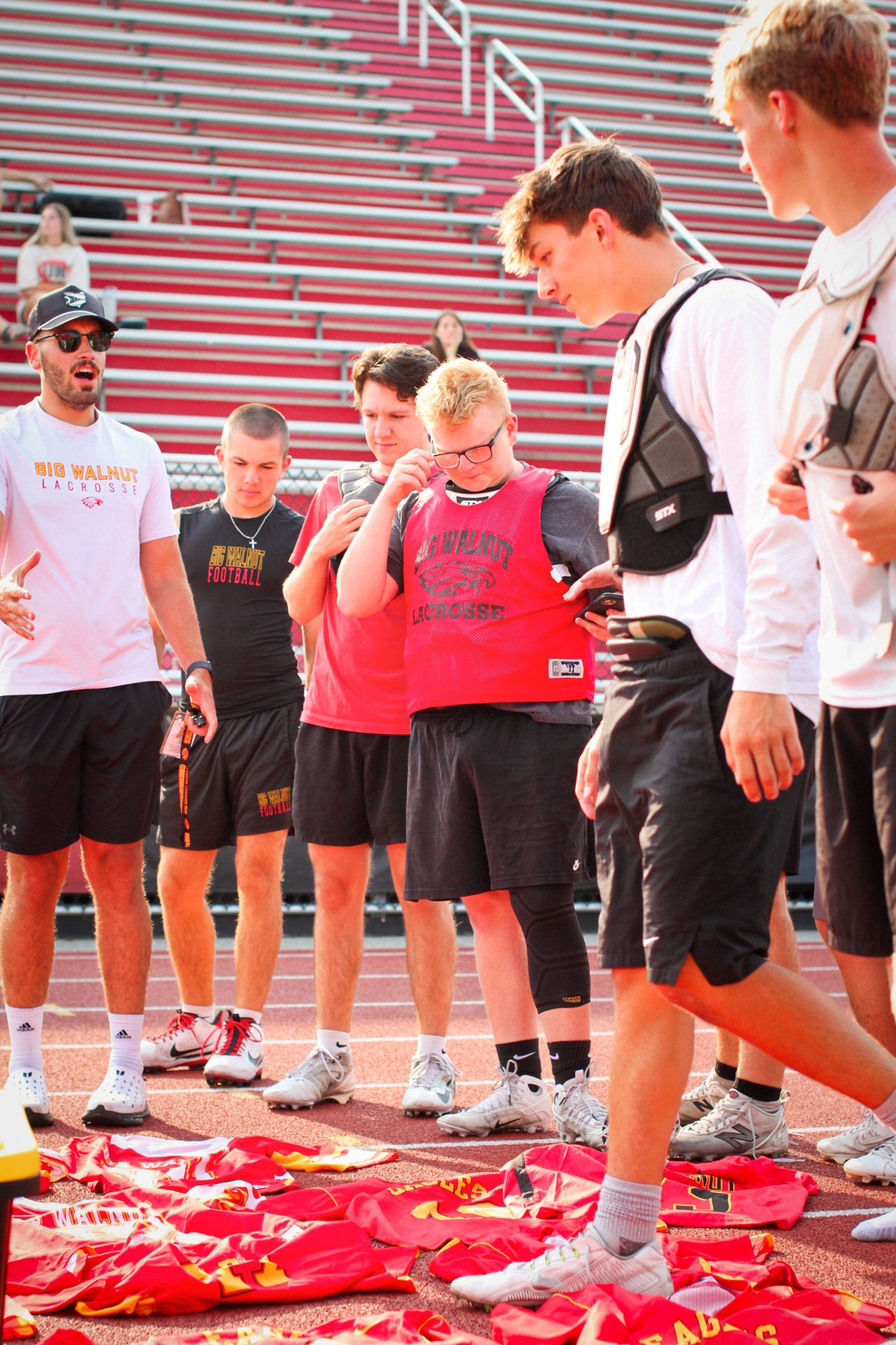 Group of people standing on a stadium field around red confetti, one covering their face in a red shirt