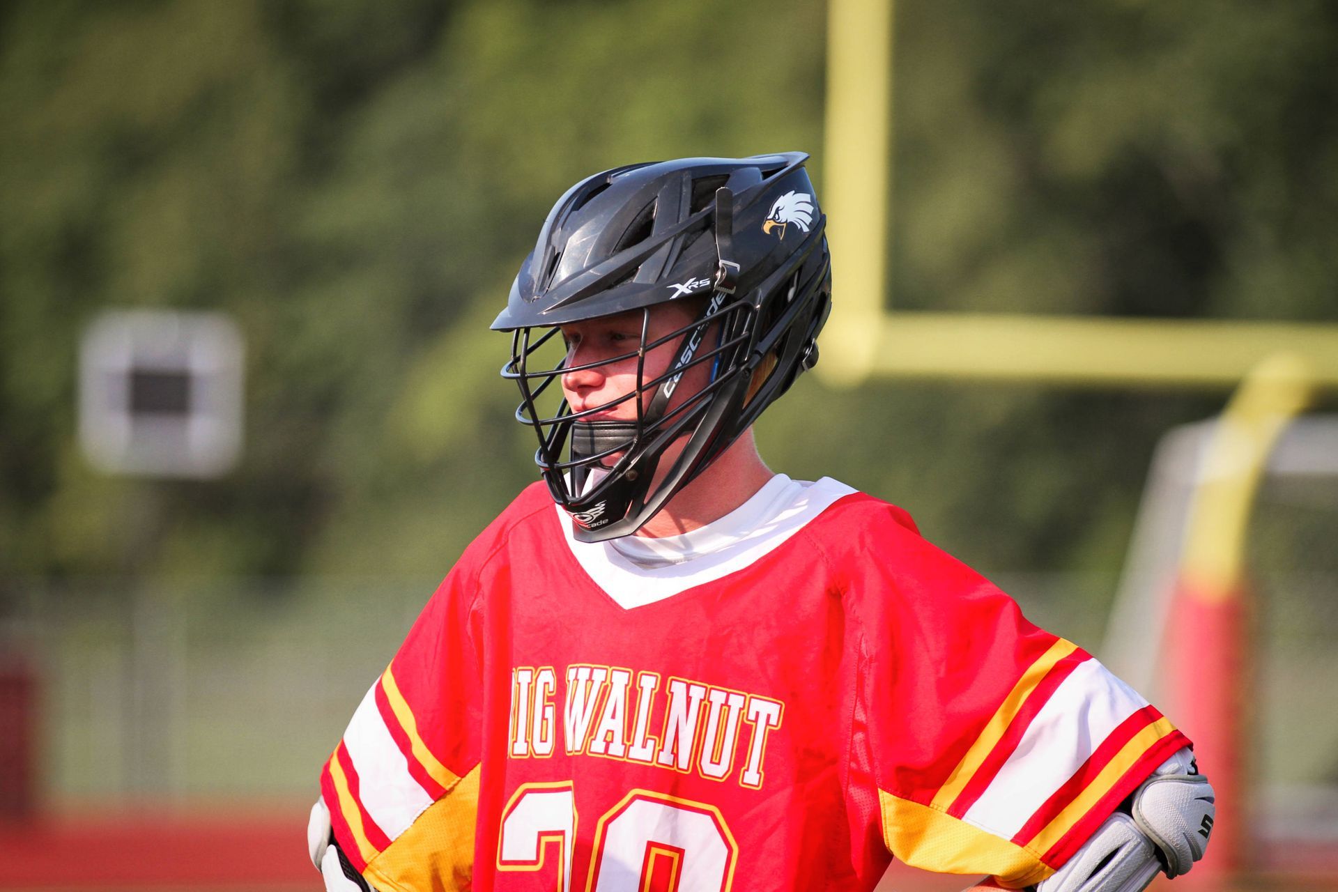 Lacrosse player in a red jersey and black helmet standing on a field
