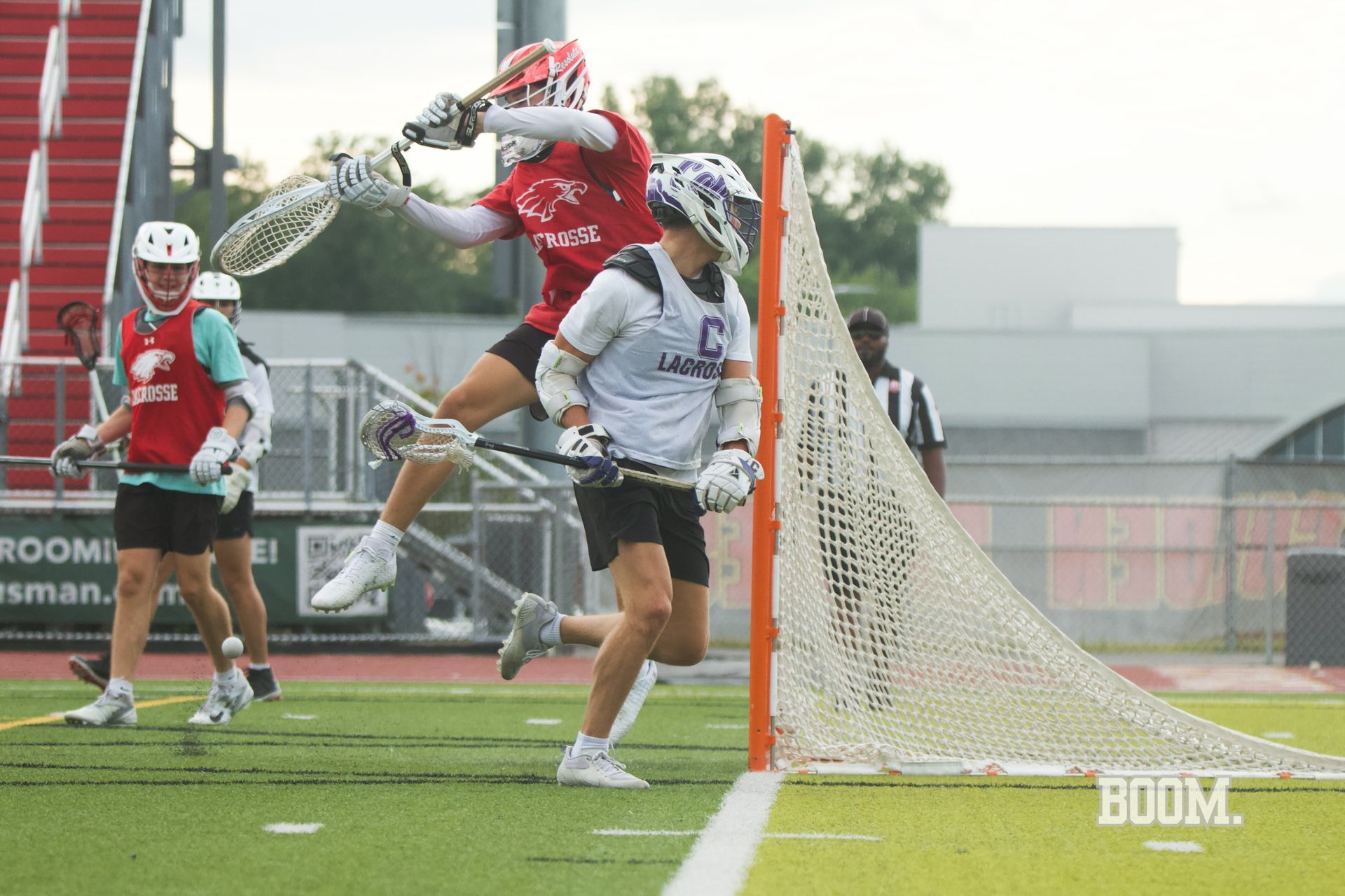 Lacrosse player in red leaps behind the goal to shoot, with defenders nearby on a foggy field.