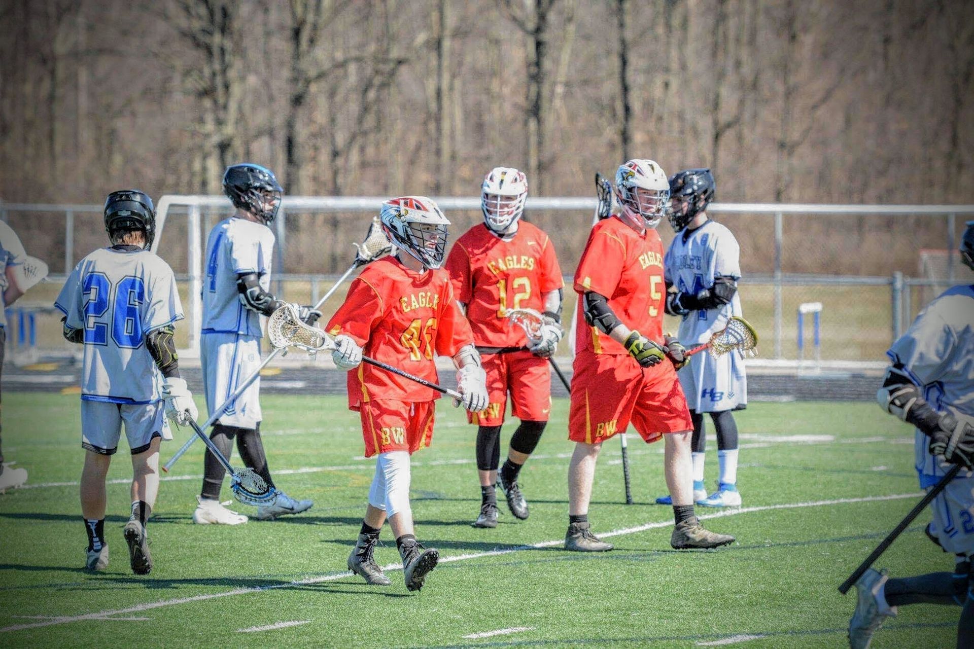 Lacrosse players in red and blue uniforms gathered on a turf field during a game pause.