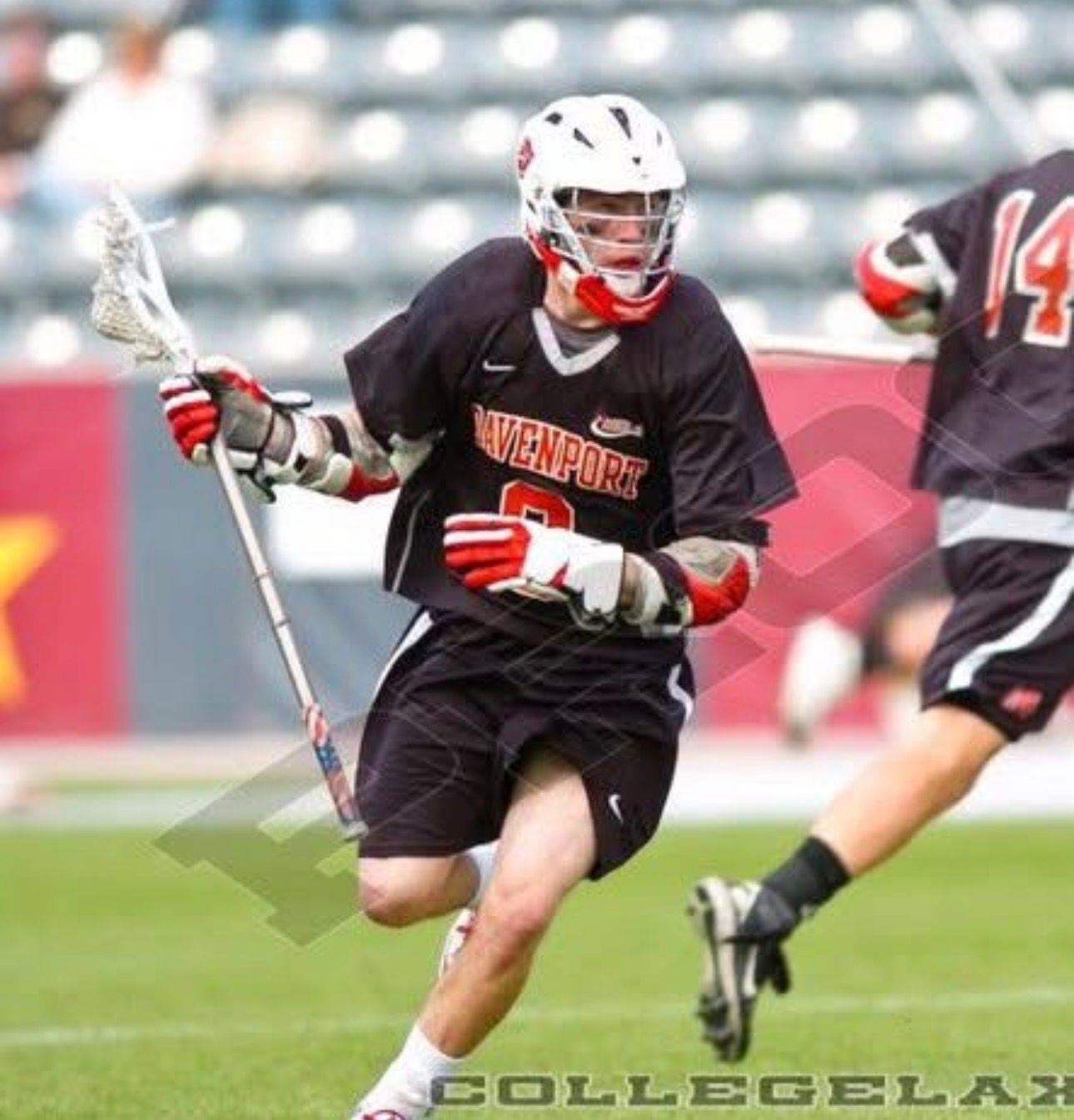Lacrosse player in black uniform and white helmet running with the ball on a field
