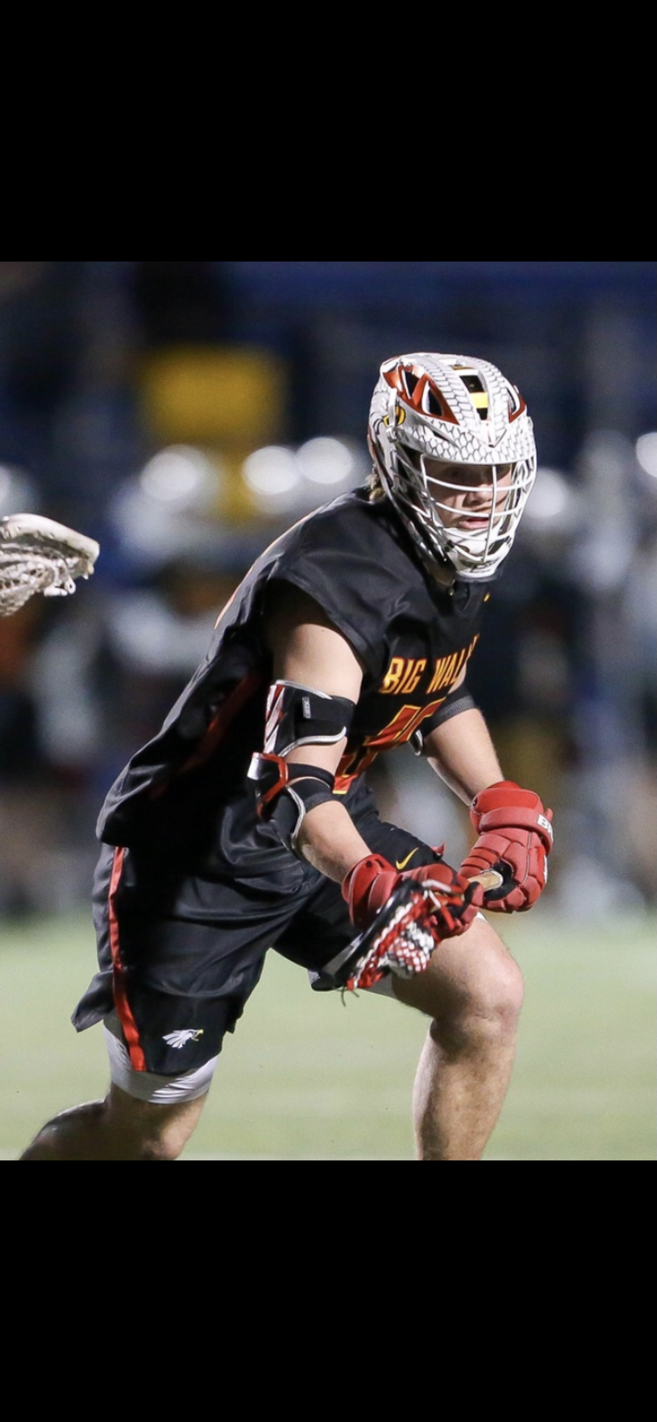 Lacrosse player in black uniform and helmet runs with the ball during a night game