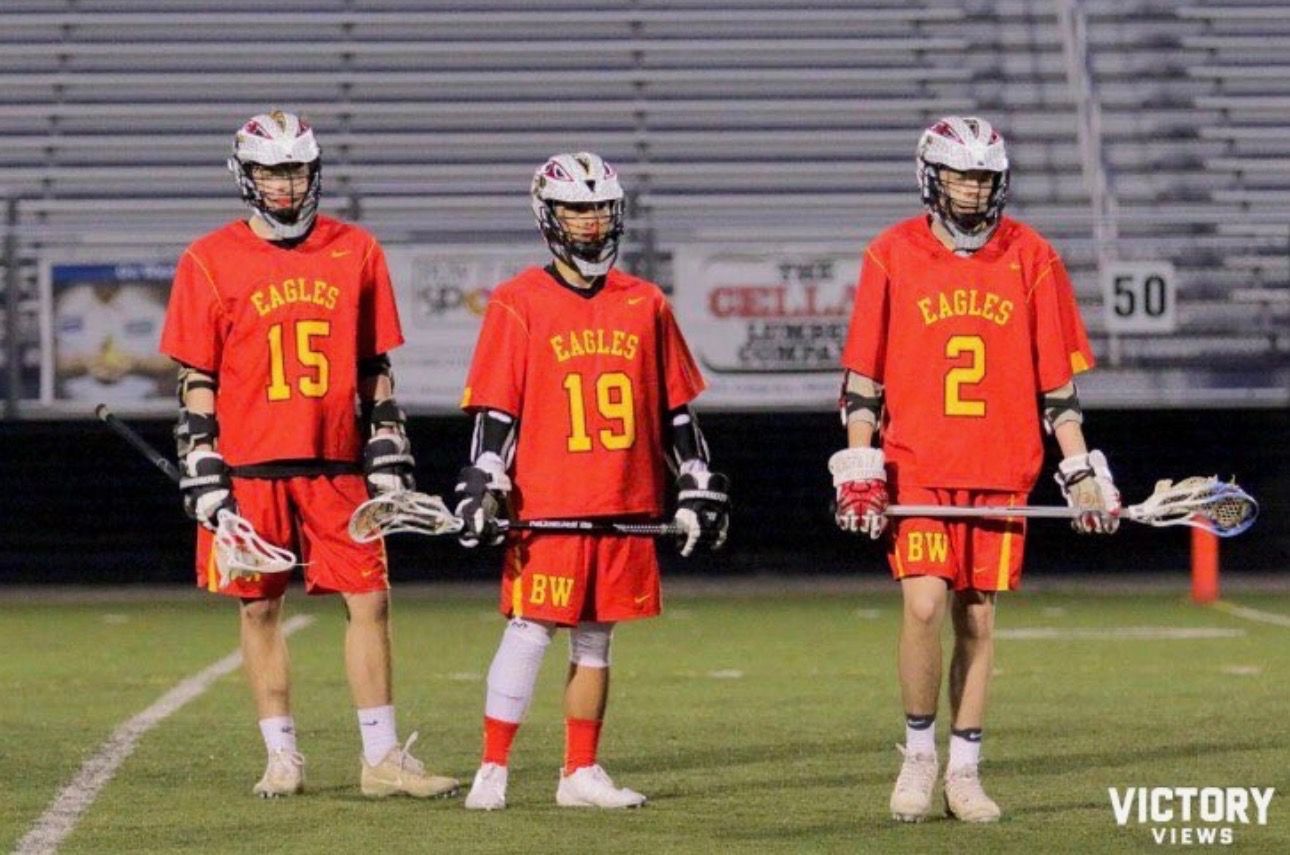 Three lacrosse players in red uniforms standing on a field at night