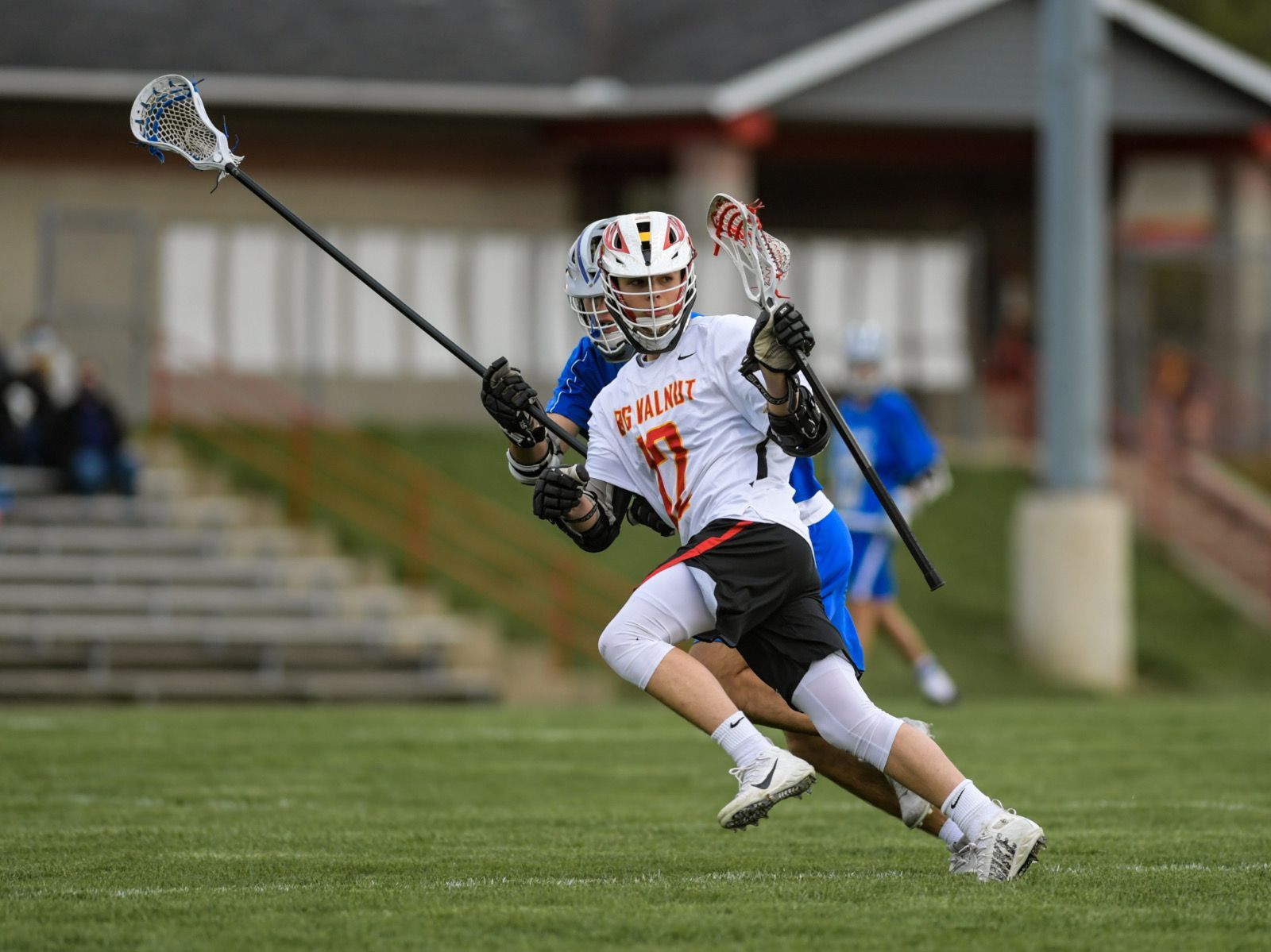 Lacrosse player in white and orange jersey running with stick on a grassy field