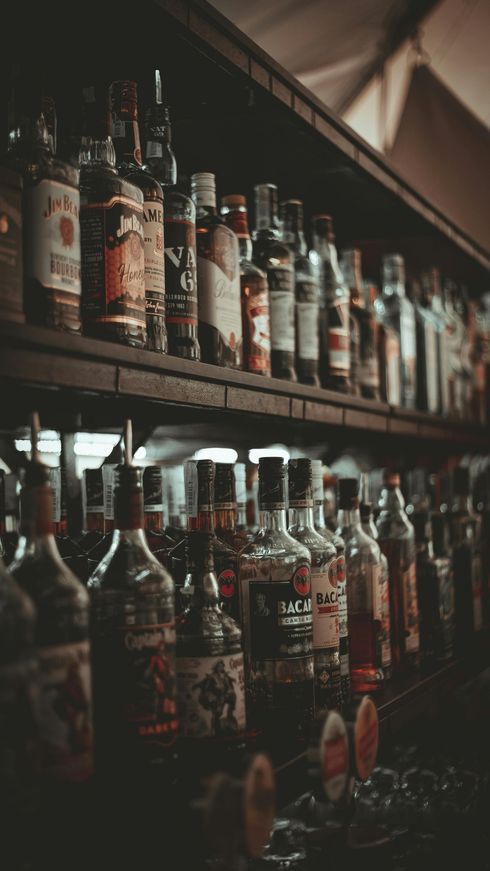 Filas de botellas de licores variados en los estantes de un bar o tienda con poca luz.