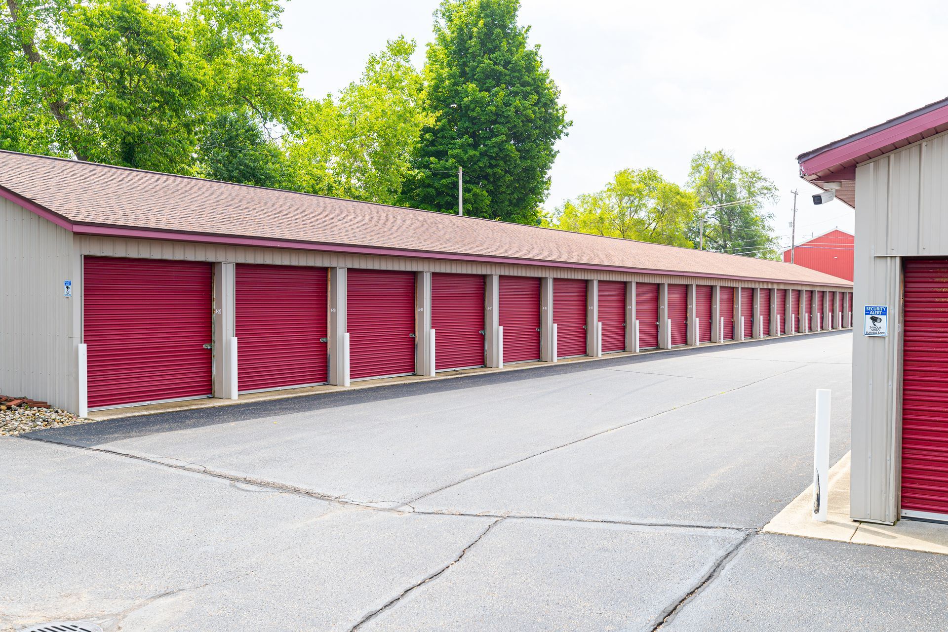 Row of red self-storage unit doors beside a paved drive with trees in the background