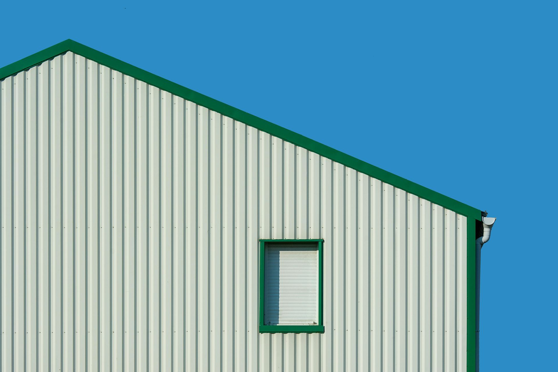 White corrugated metal building with green trim and a single window, against a bright blue sky.