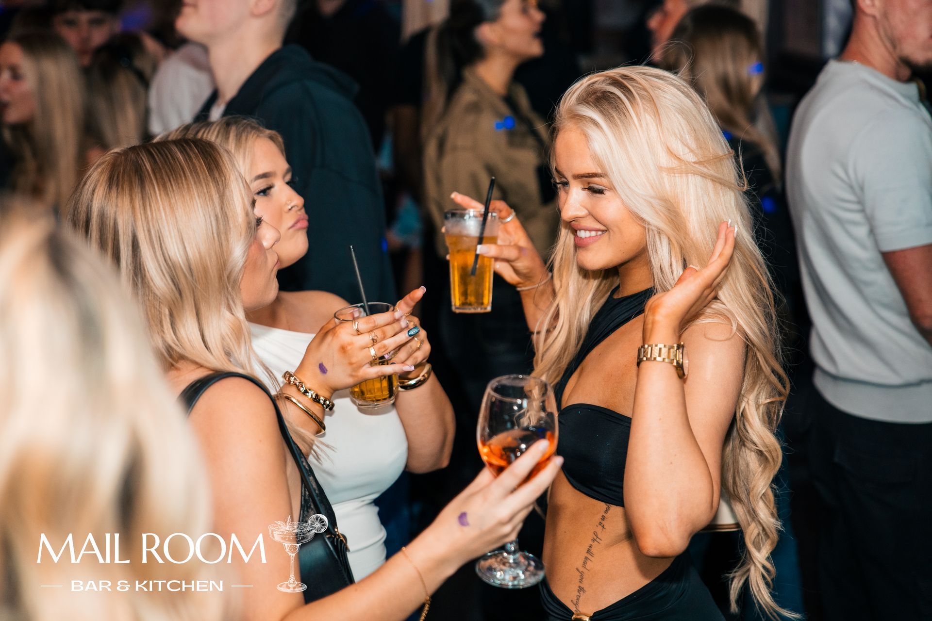 A group of women are standing in a crowd holding drinks.