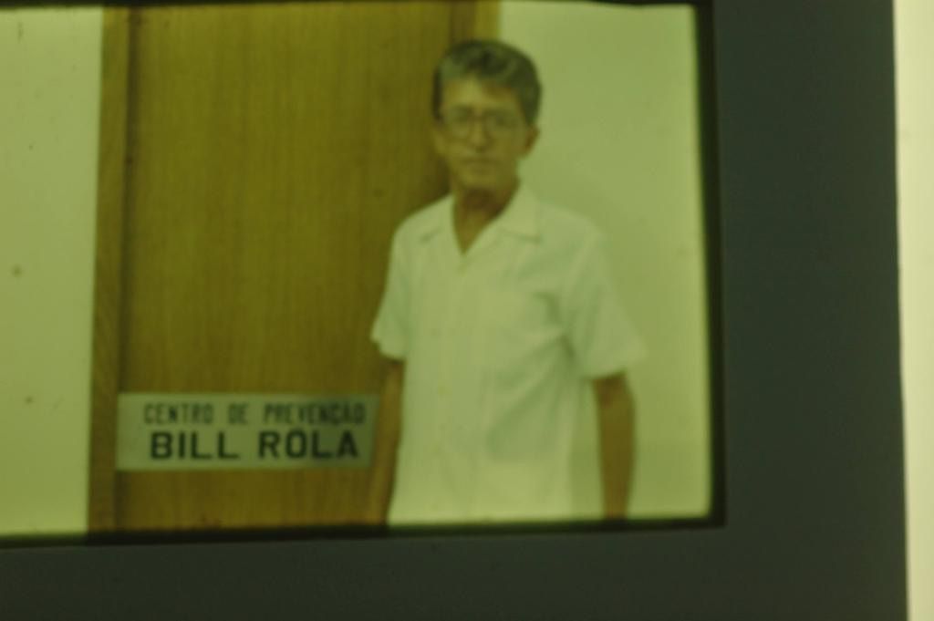 Uma pessoa vestindo uma camisa branca de colarinho está ao lado de uma porta de madeira com a inscrição 